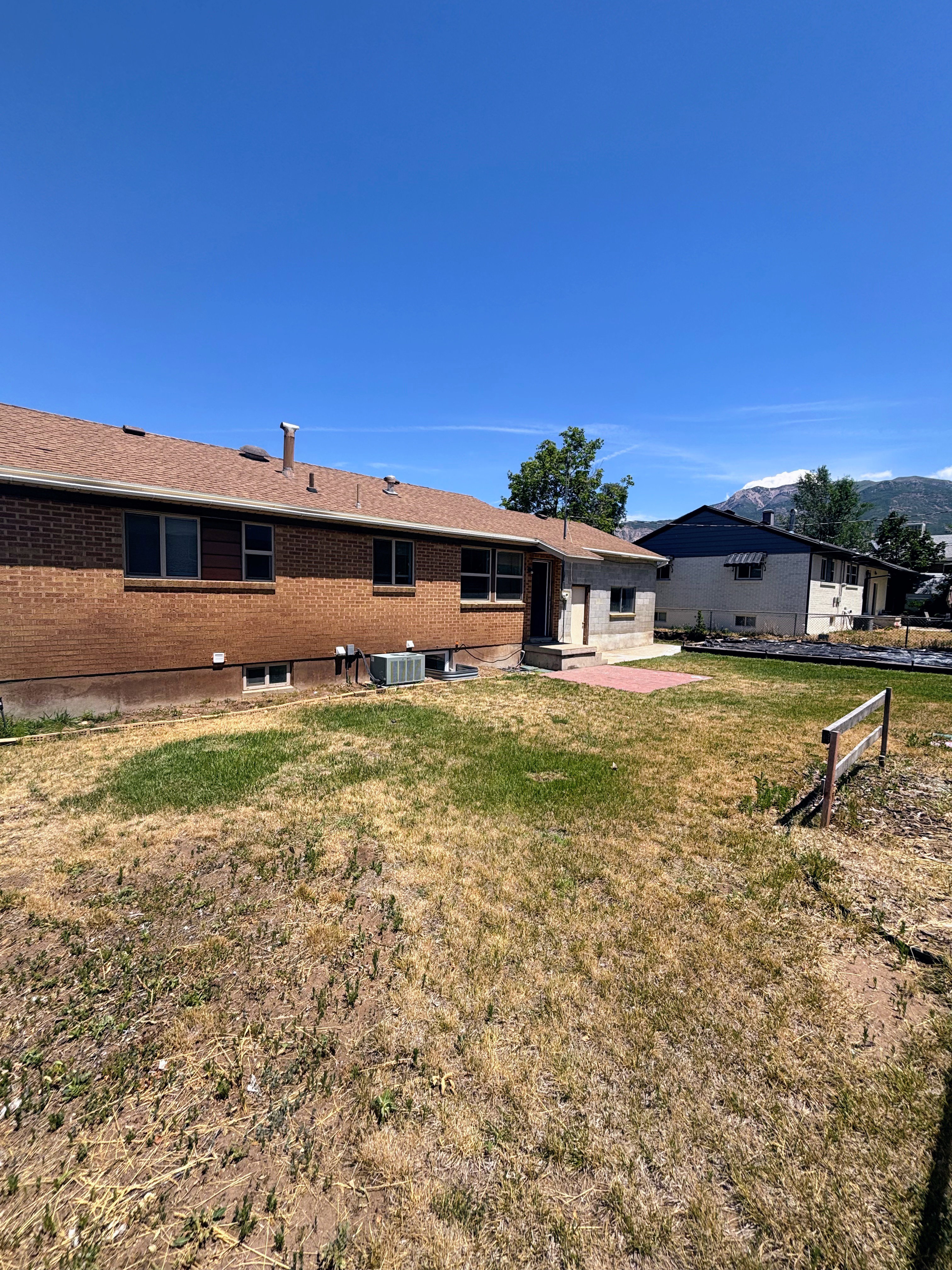 Expansive backyard space with a partial brick exterior, a paved patio area, and a visible air conditioning unit.