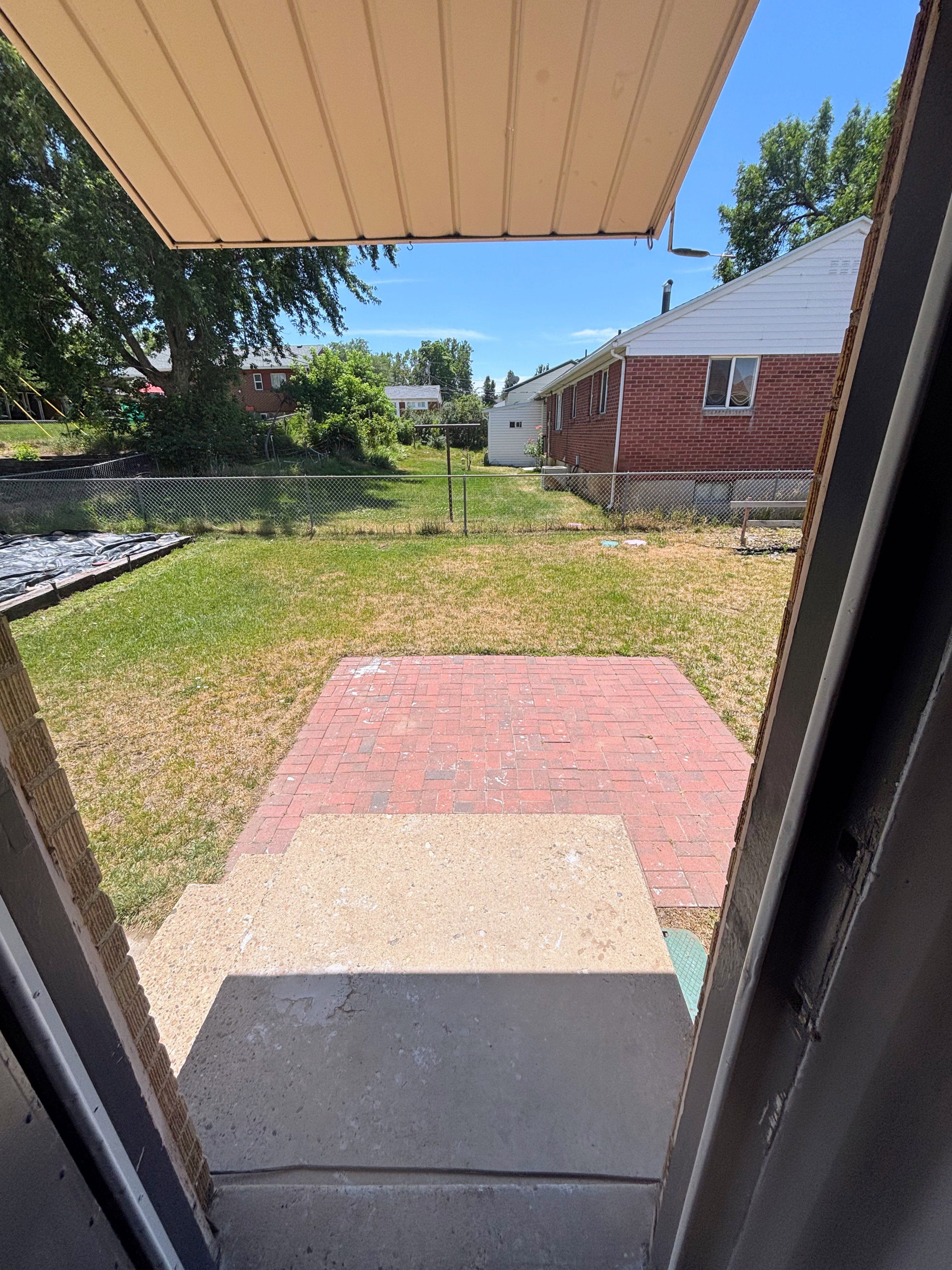 Backyard - Outdoor living space featuring a concrete patio, brick paver extension, and a partial awning overhead.