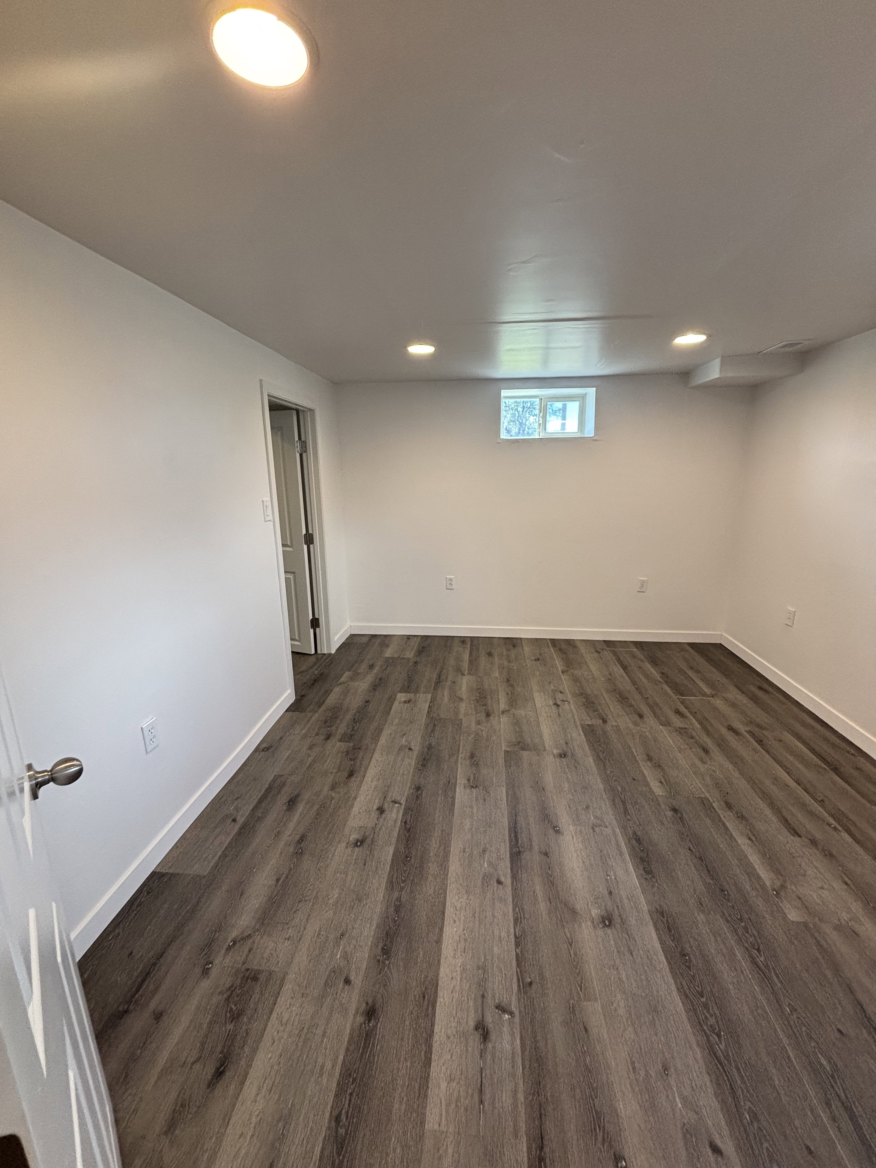 Spacious room featuring wood-finish flooring, recessed lighting, white walls, and a visible window.