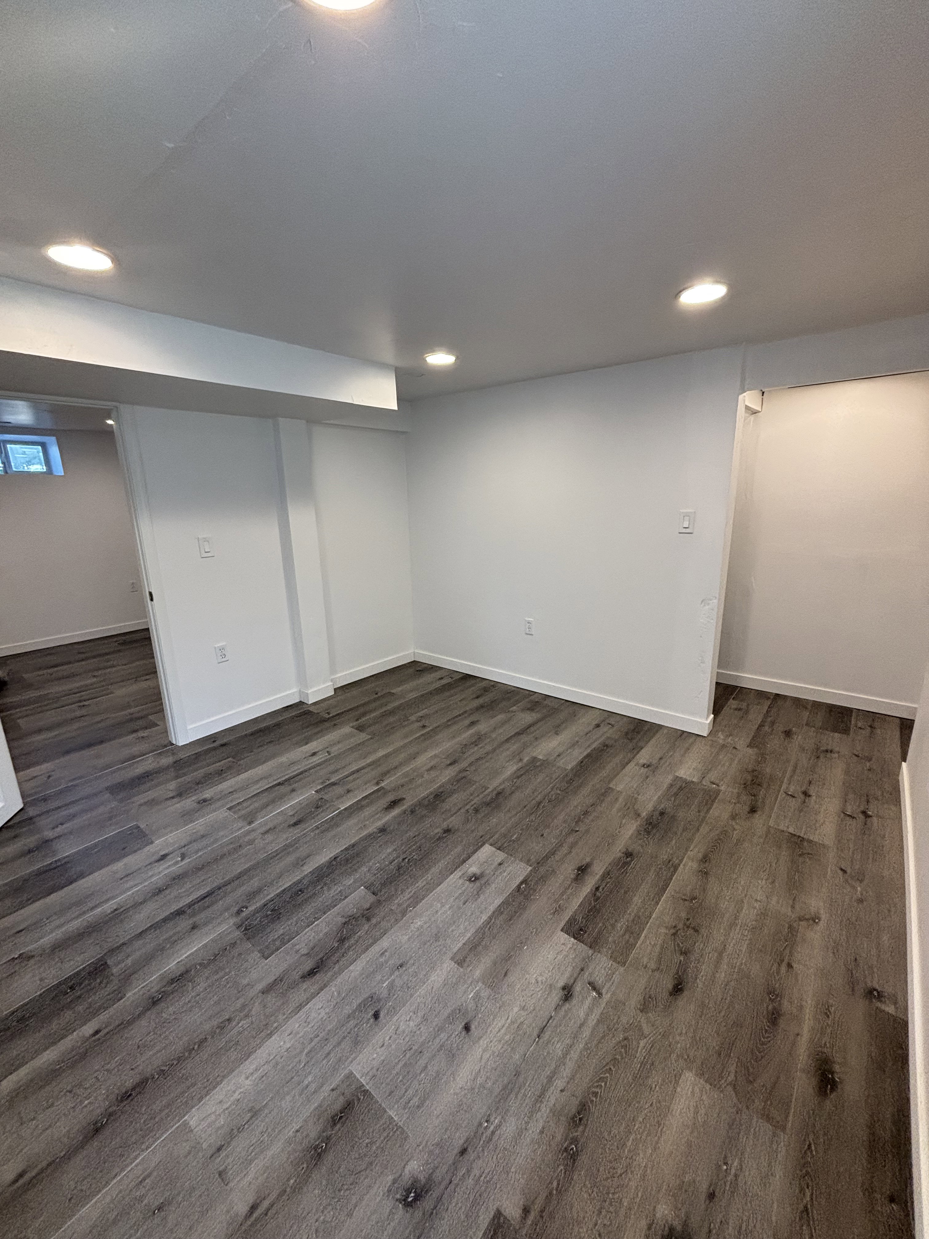 Spacious room featuring wood-finish flooring, recessed lighting, white walls, and white baseboards.