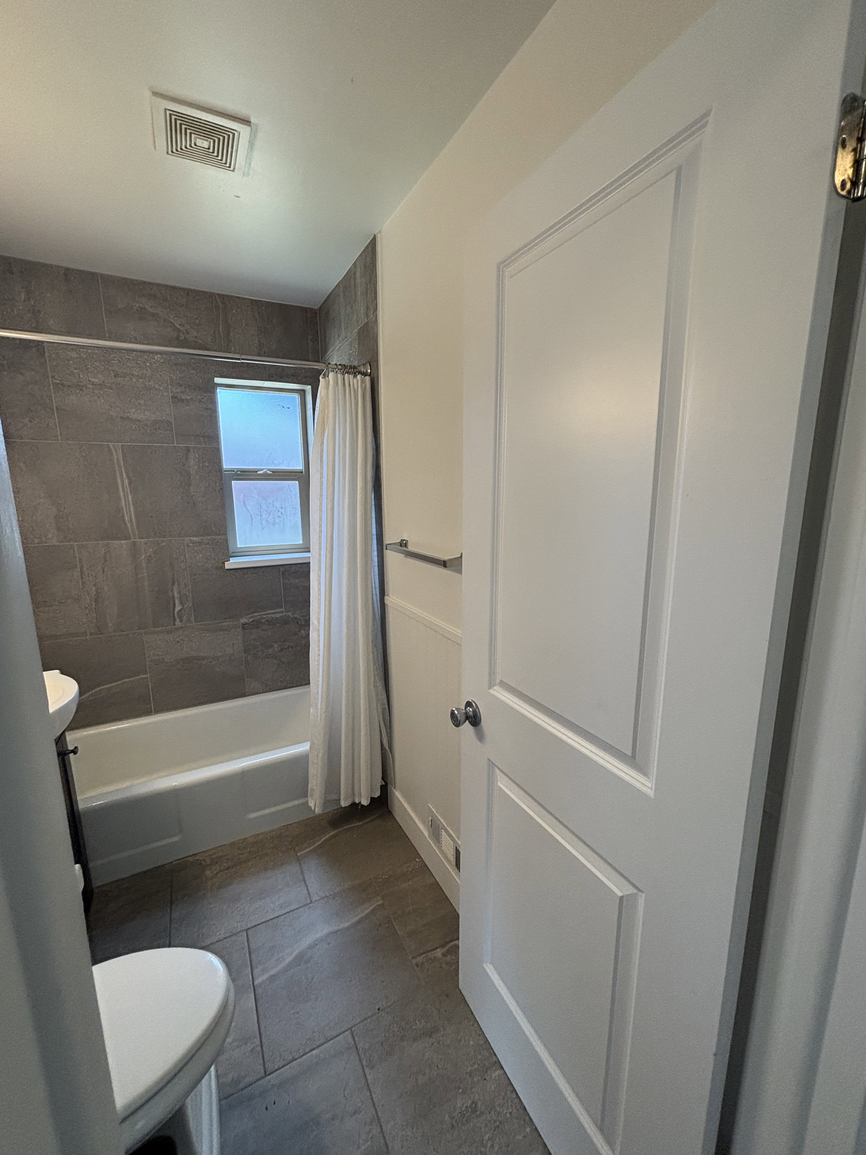 Bathroom featuring a white tub, dark grey large format tile shower surround, and a coordinating tile floor.