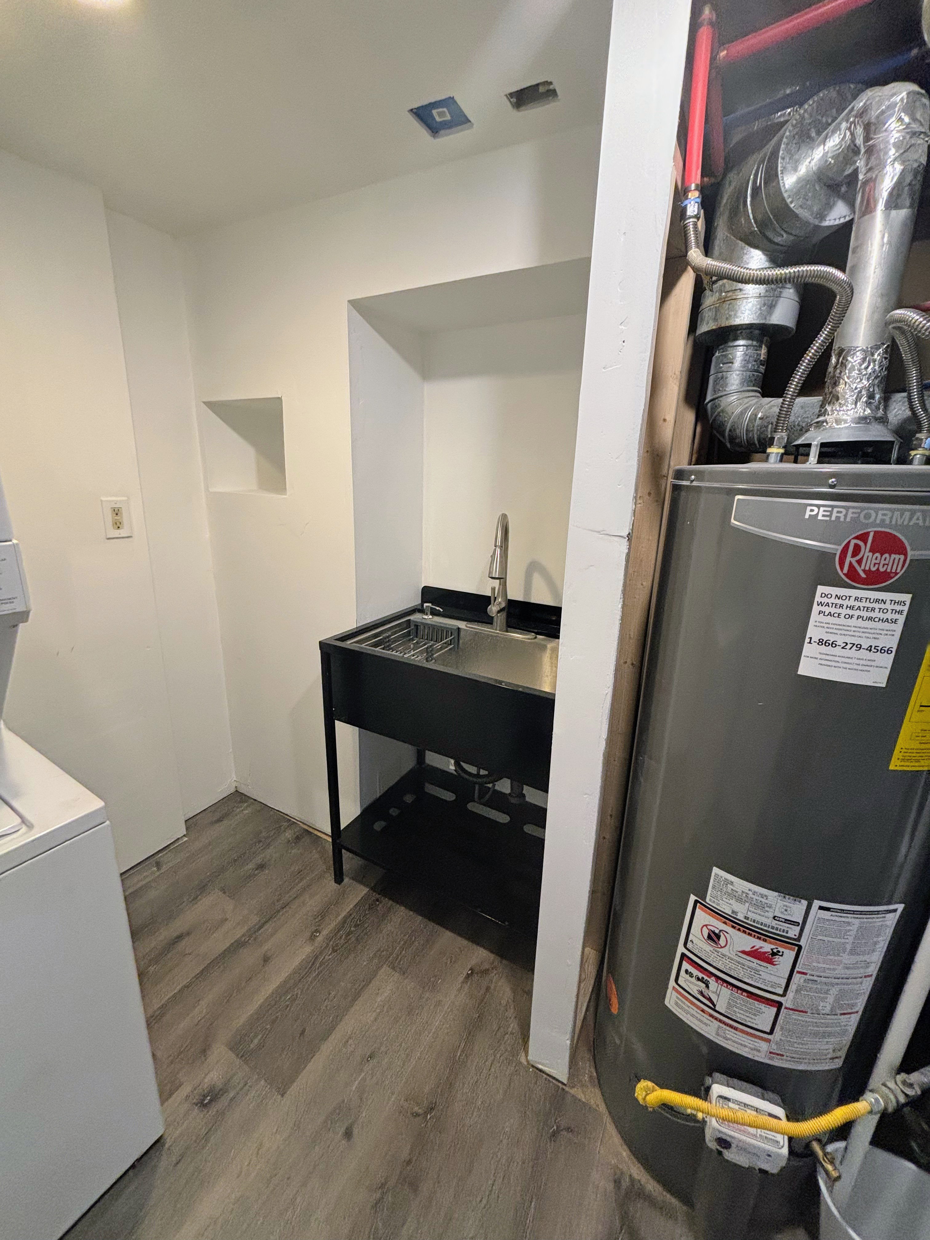 Utility area featuring a stainless steel sink with a modern faucet, wood-finish flooring, recessed wall niche, and white painted walls.