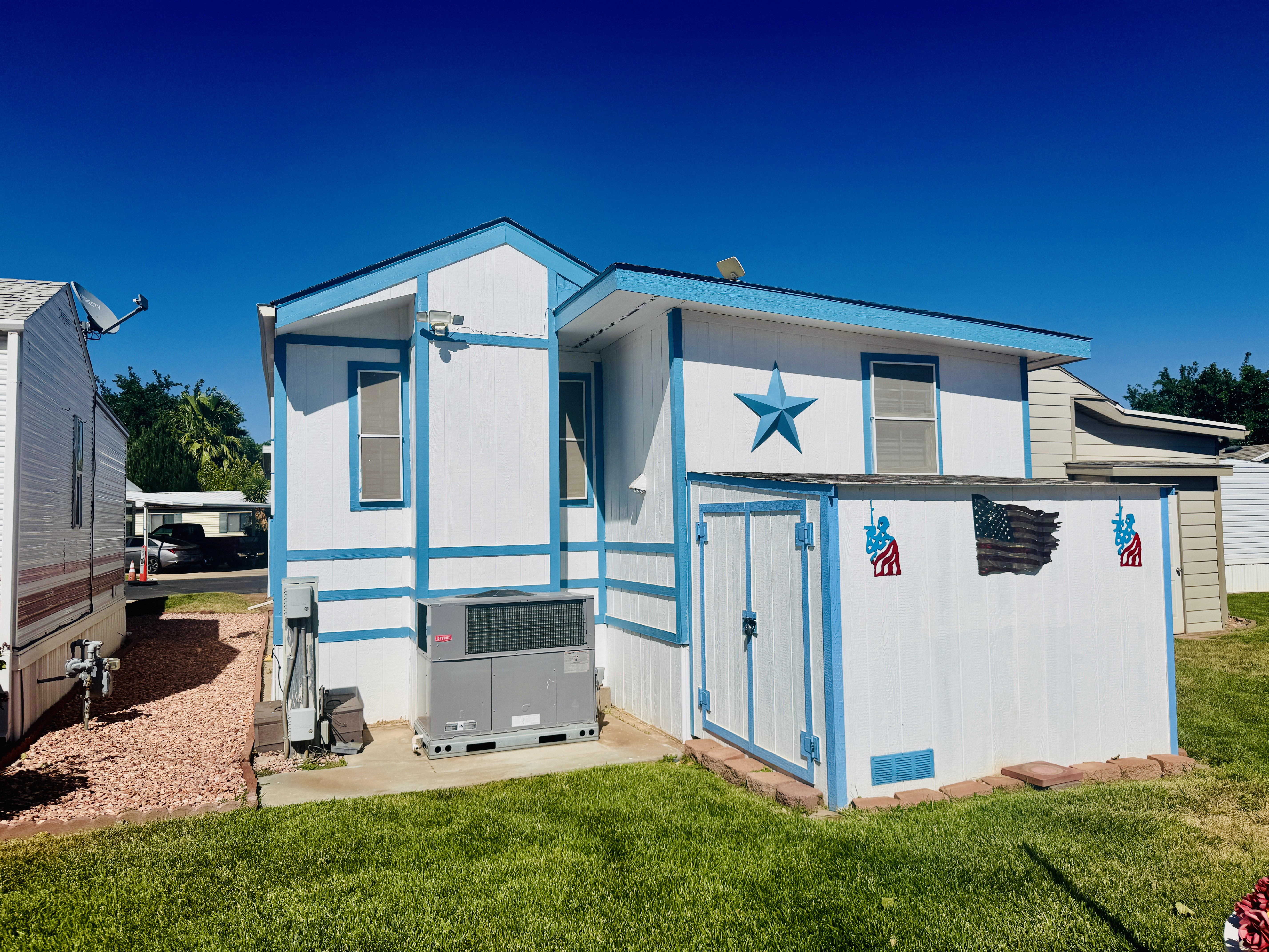 White exterior with blue trim accents, featuring an attached storage shed with double doors