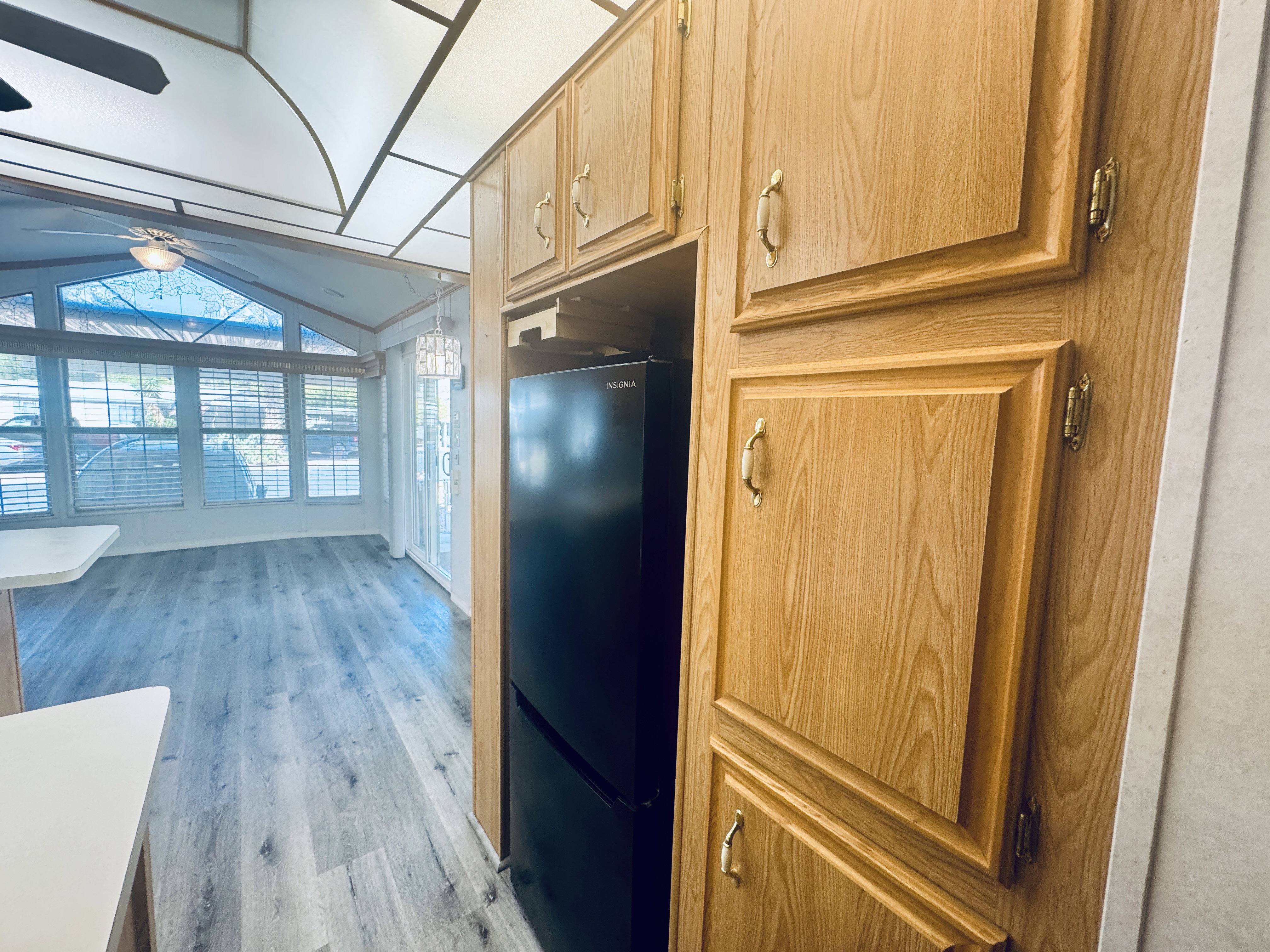 Light wood-finish cabinetry with golden hardware, a black refrigerator, and light wood-finish flooring