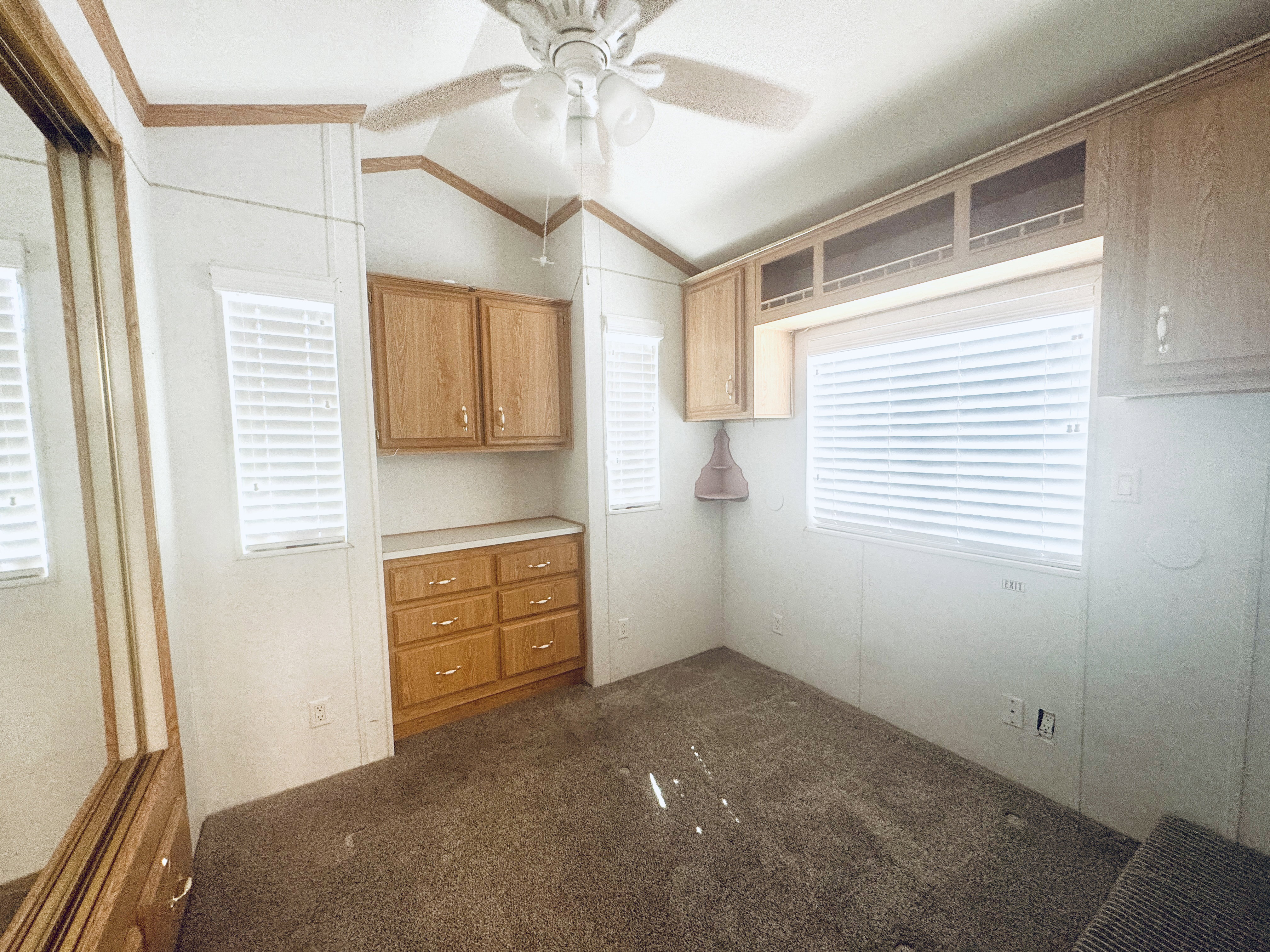 Room featuring multiple windows with blinds, a built-in ceiling fan, and extensive wood-finish cabinetry including a dresser and overhead storage