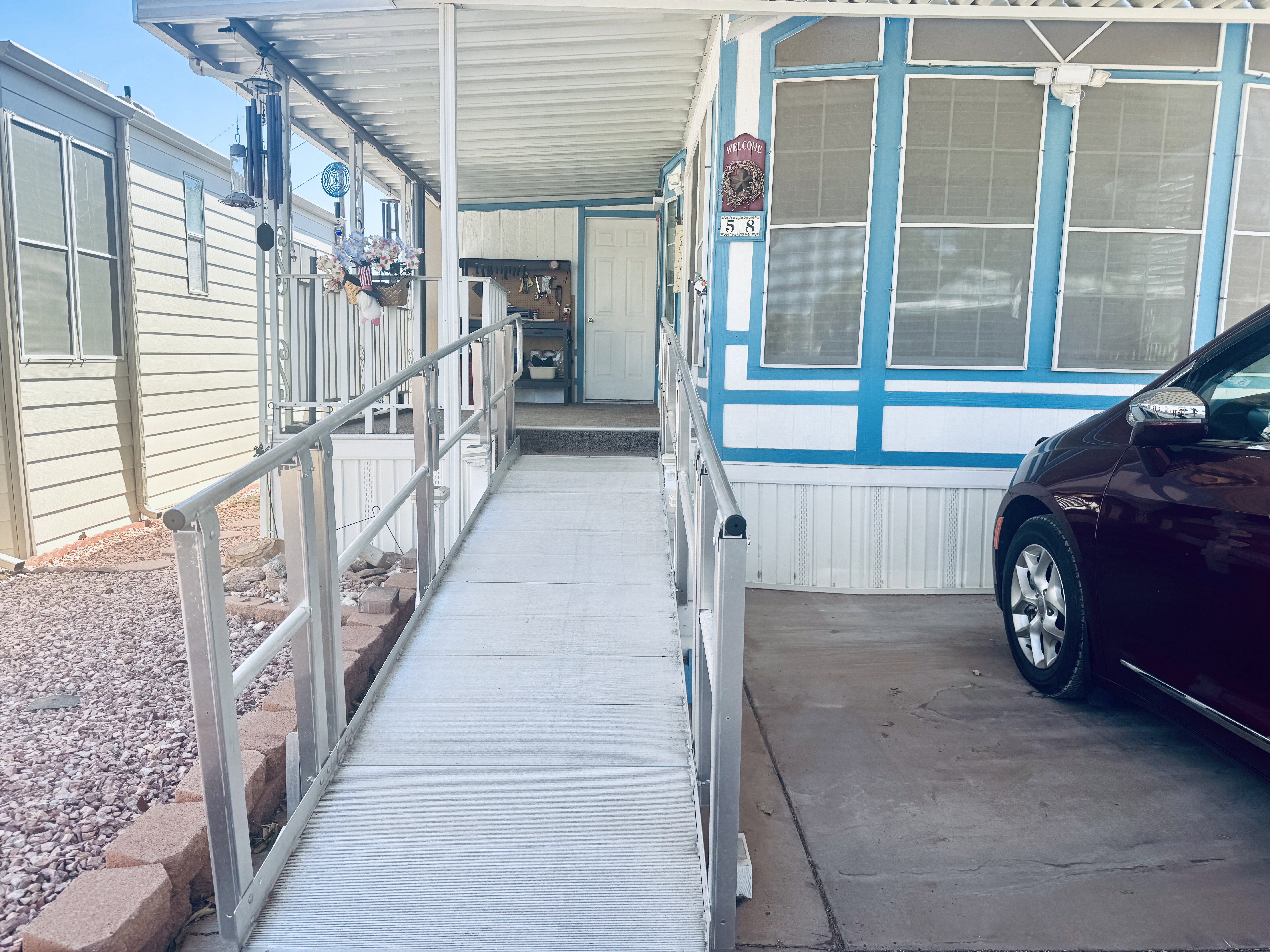 Exterior entrance featuring a covered porch, aluminum ramp with handrails, and a dedicated carport space