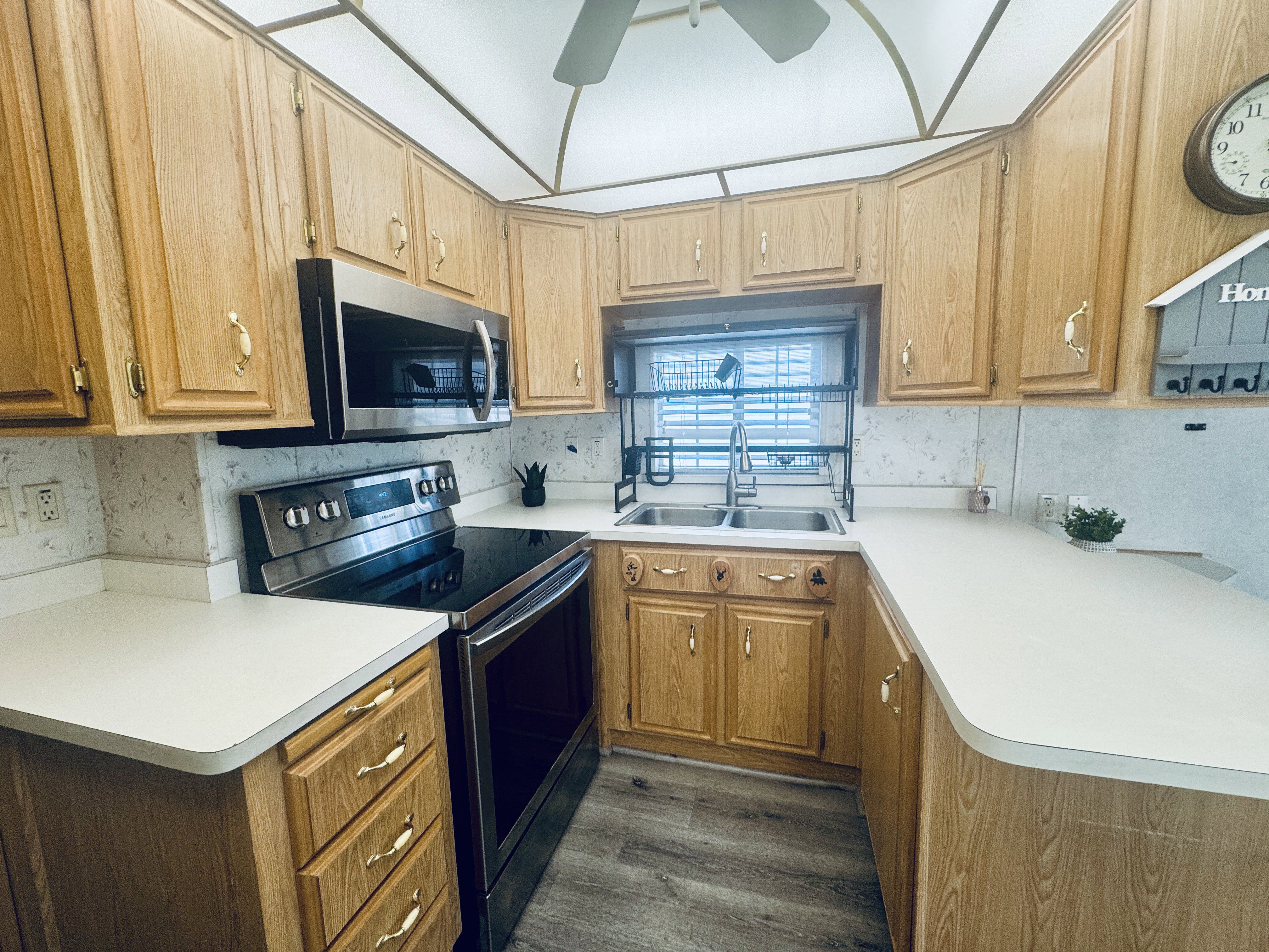Kitchen featuring wood-finish cabinetry, light-toned countertops, a stainless steel electric range, an over-range microwave, and a double basin sink