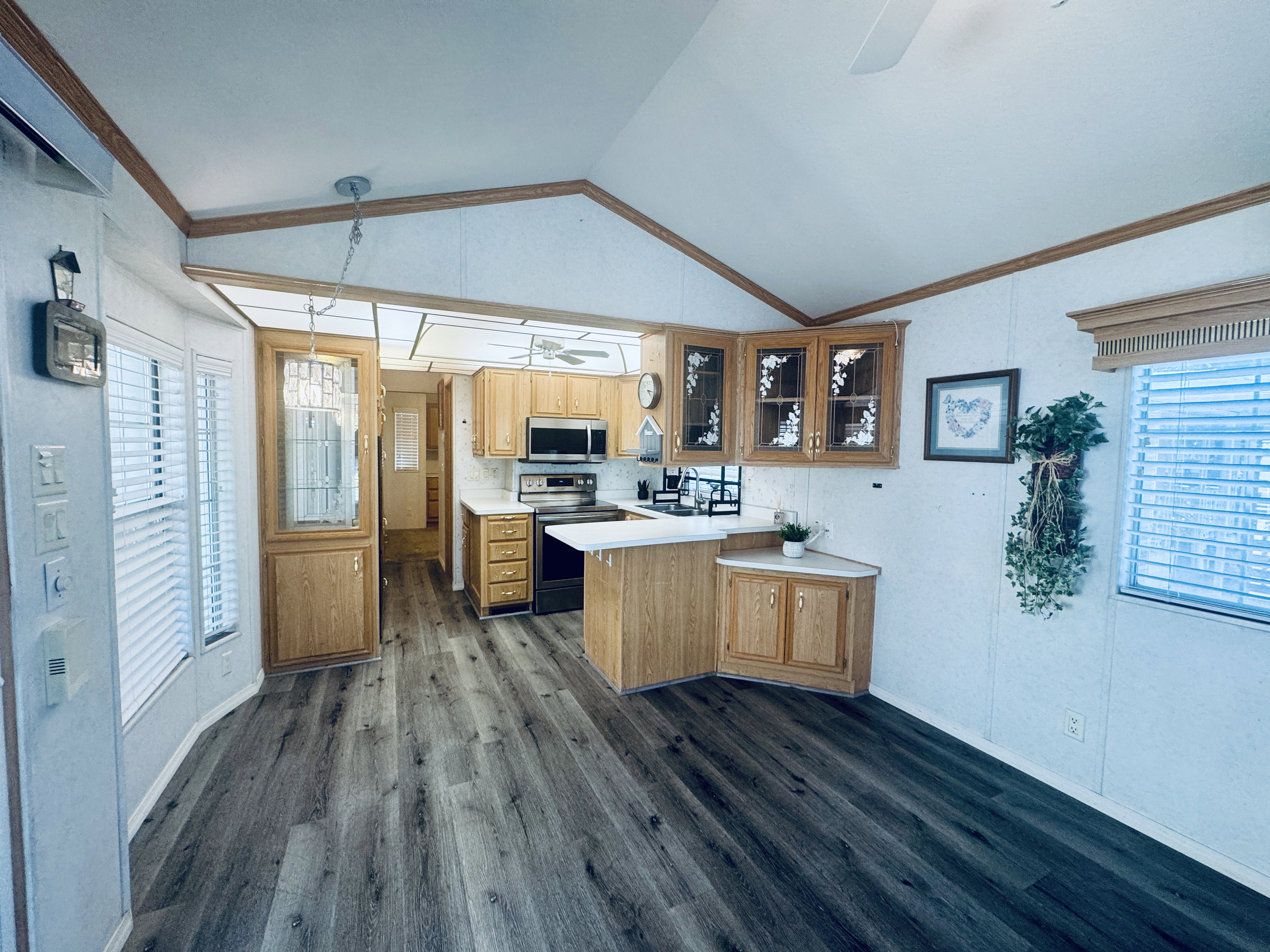 Kitchen with stainless steel appliances, wood-finish flooring, vaulted ceiling, wood cabinetry, and a built-in microwave
