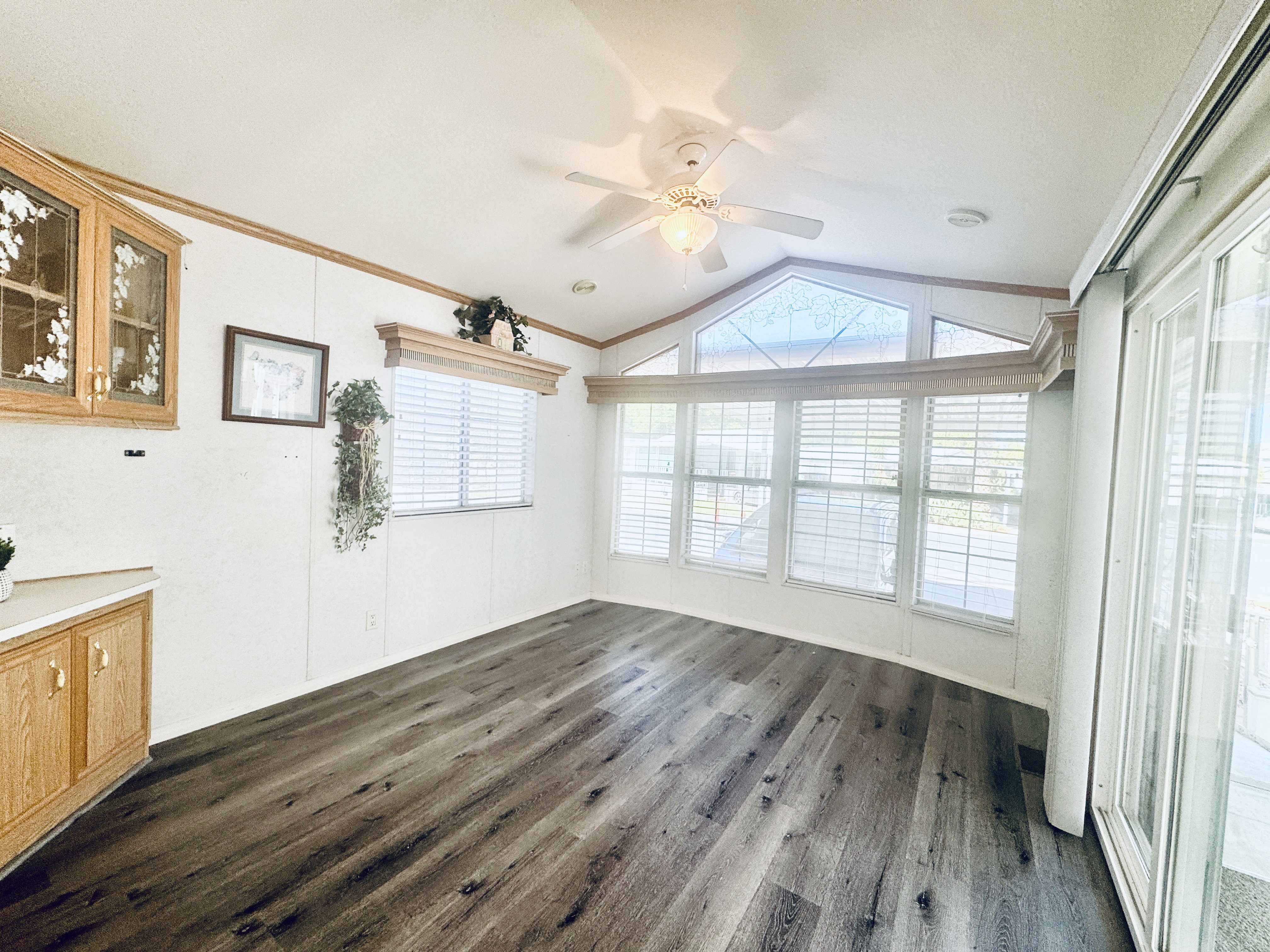 Spacious room featuring wood-finish flooring, a ceiling fan with light fixture, and extensive natural light from multiple windows