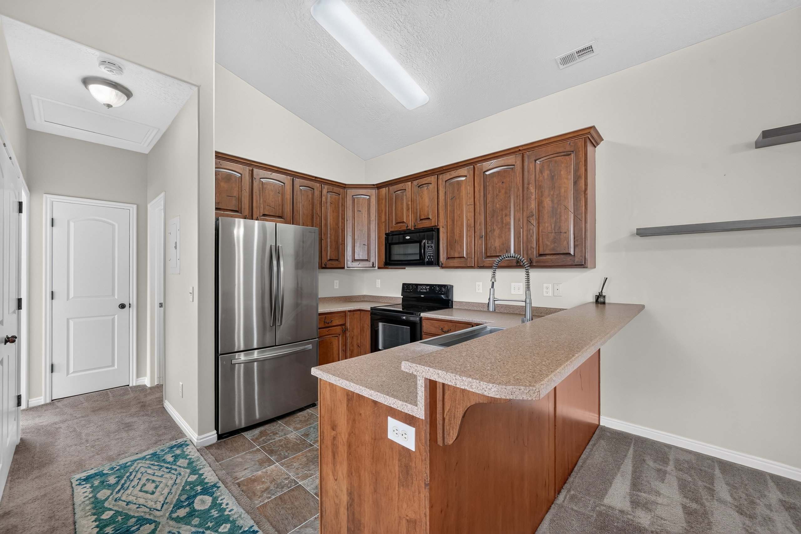 Kitchen featuring wood-finish cabinetry, stainless steel refrigerator, black range, black built-in microwave, and a breakfast bar with a single-basin sink and brushed nickel faucet