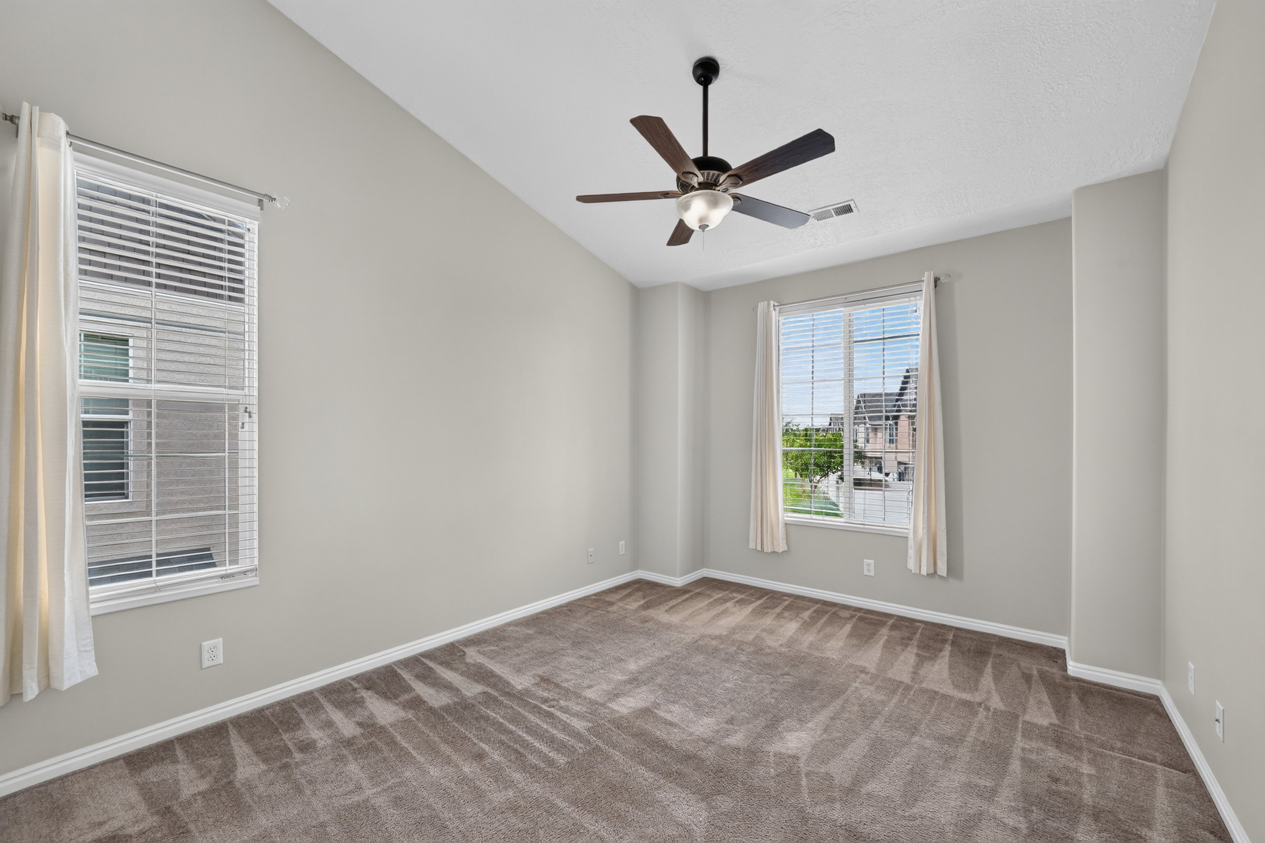 Spacious room featuring vaulted ceilings, a ceiling fan with light fixture, and plush carpet flooring