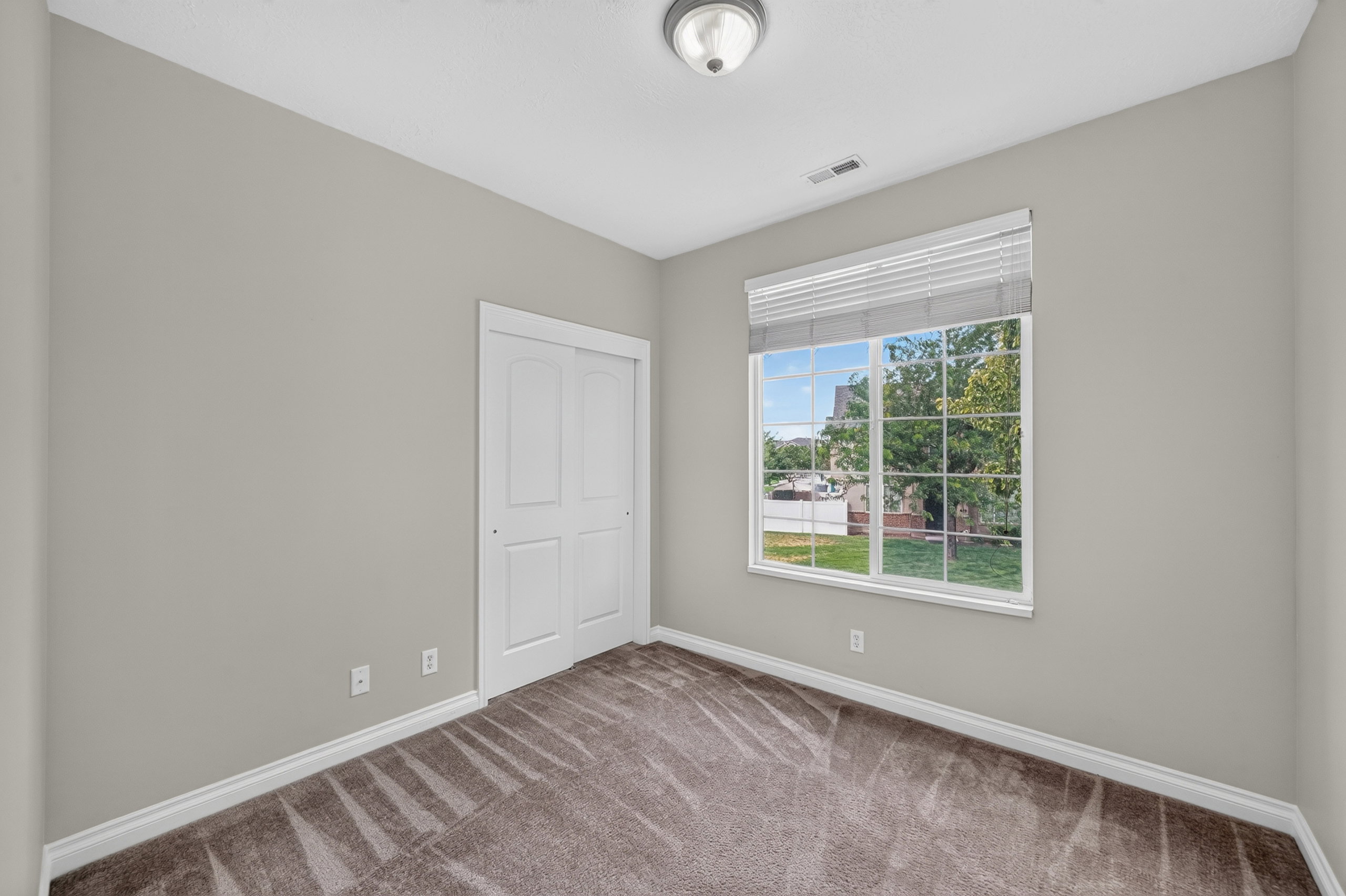 Carpeted room featuring a large window with horizontal blinds, a white bi-fold closet door, neutral wall paint, and white baseboards