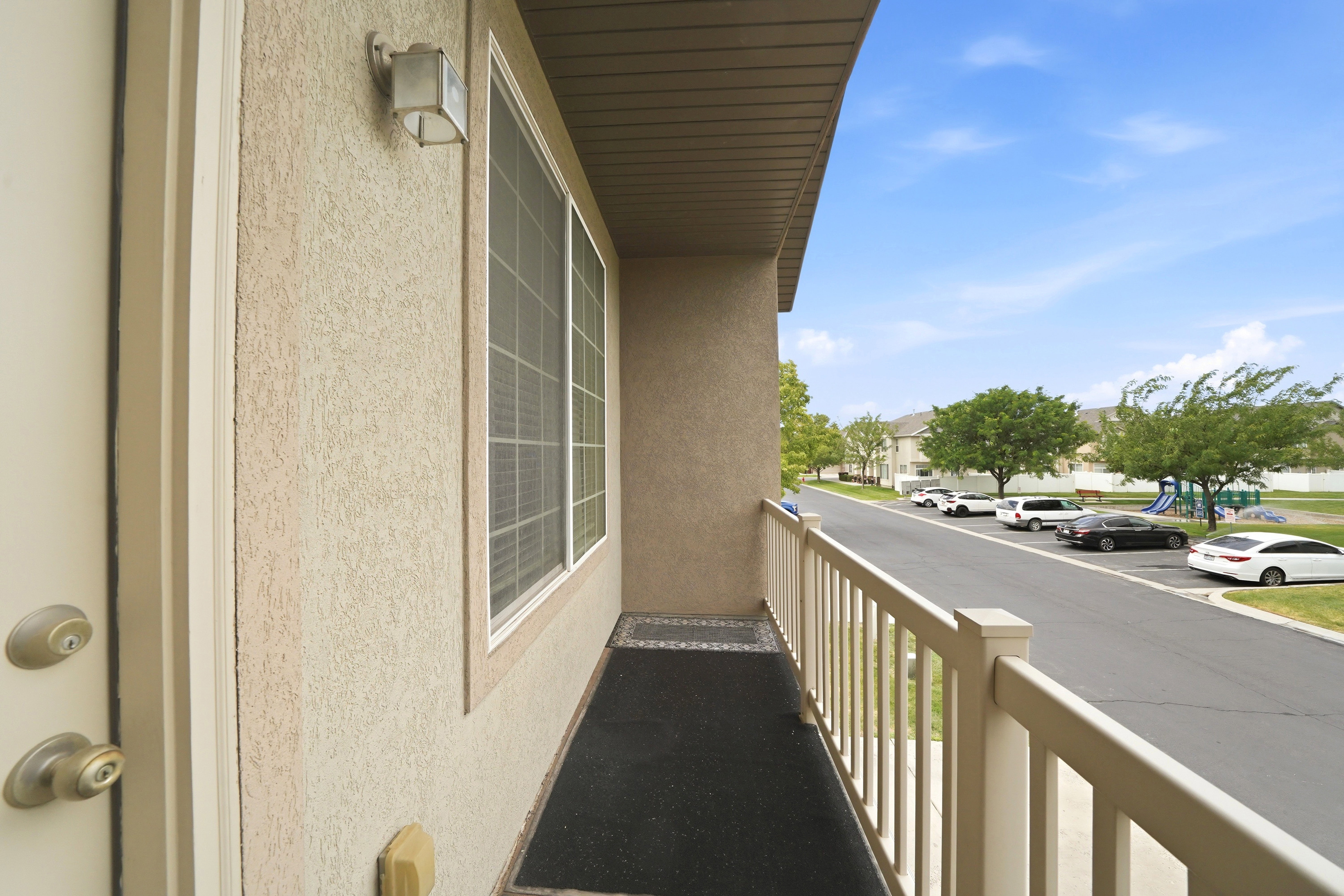 Exterior balcony with textured stucco siding, white window trim, and a white railing