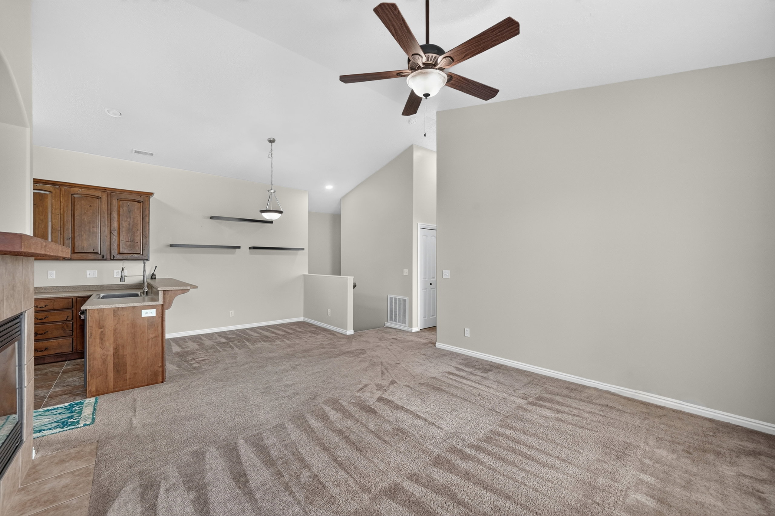 Spacious living area featuring vaulted ceilings, a ceiling fan with light, a built-in wet bar with wood cabinetry and countertop, a fireplace with a tile surround, and carpeted flooring