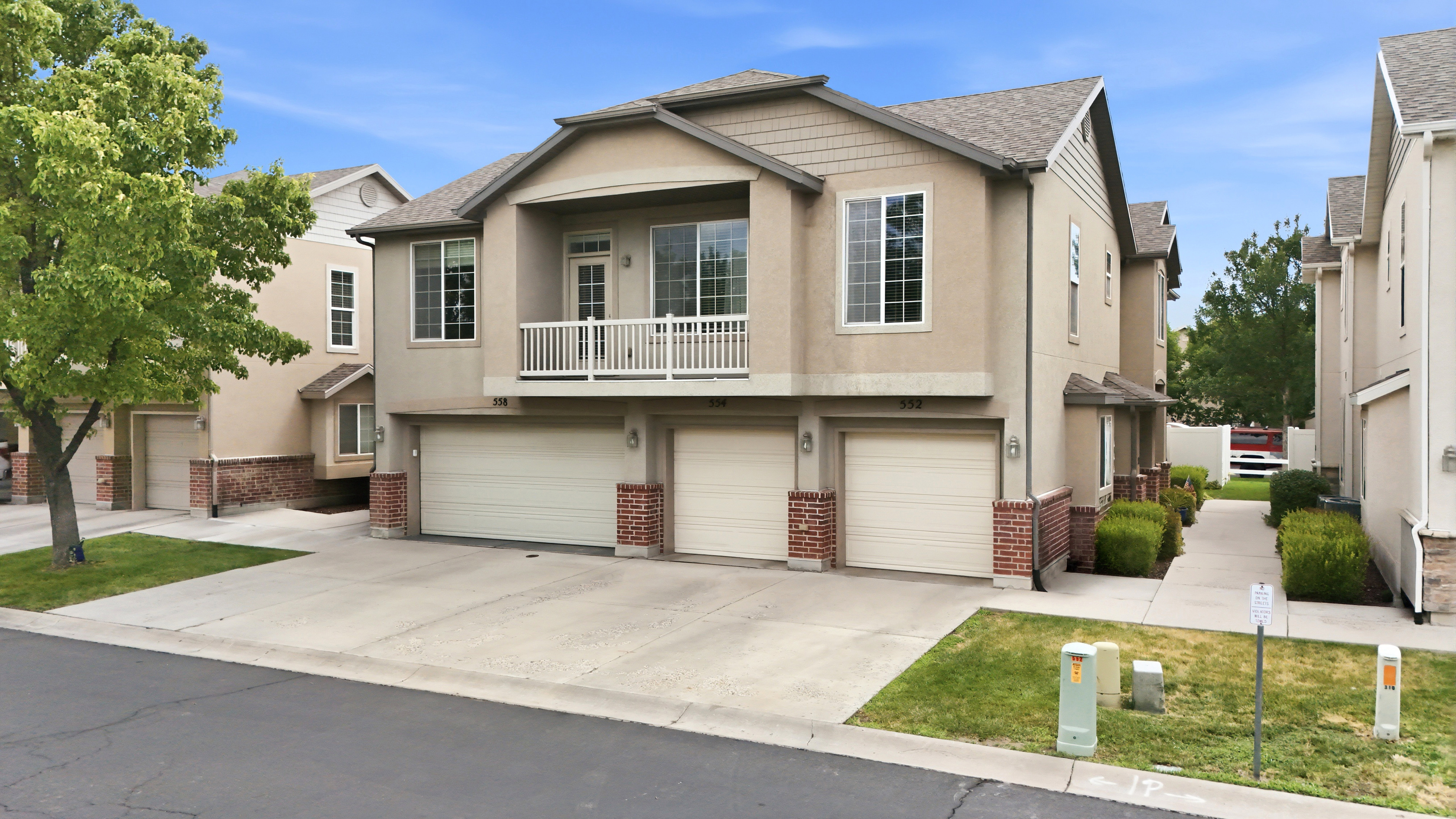 Multi-level townhome featuring a stucco and brick exterior, attached garages, and a private second-story balcony with white railing