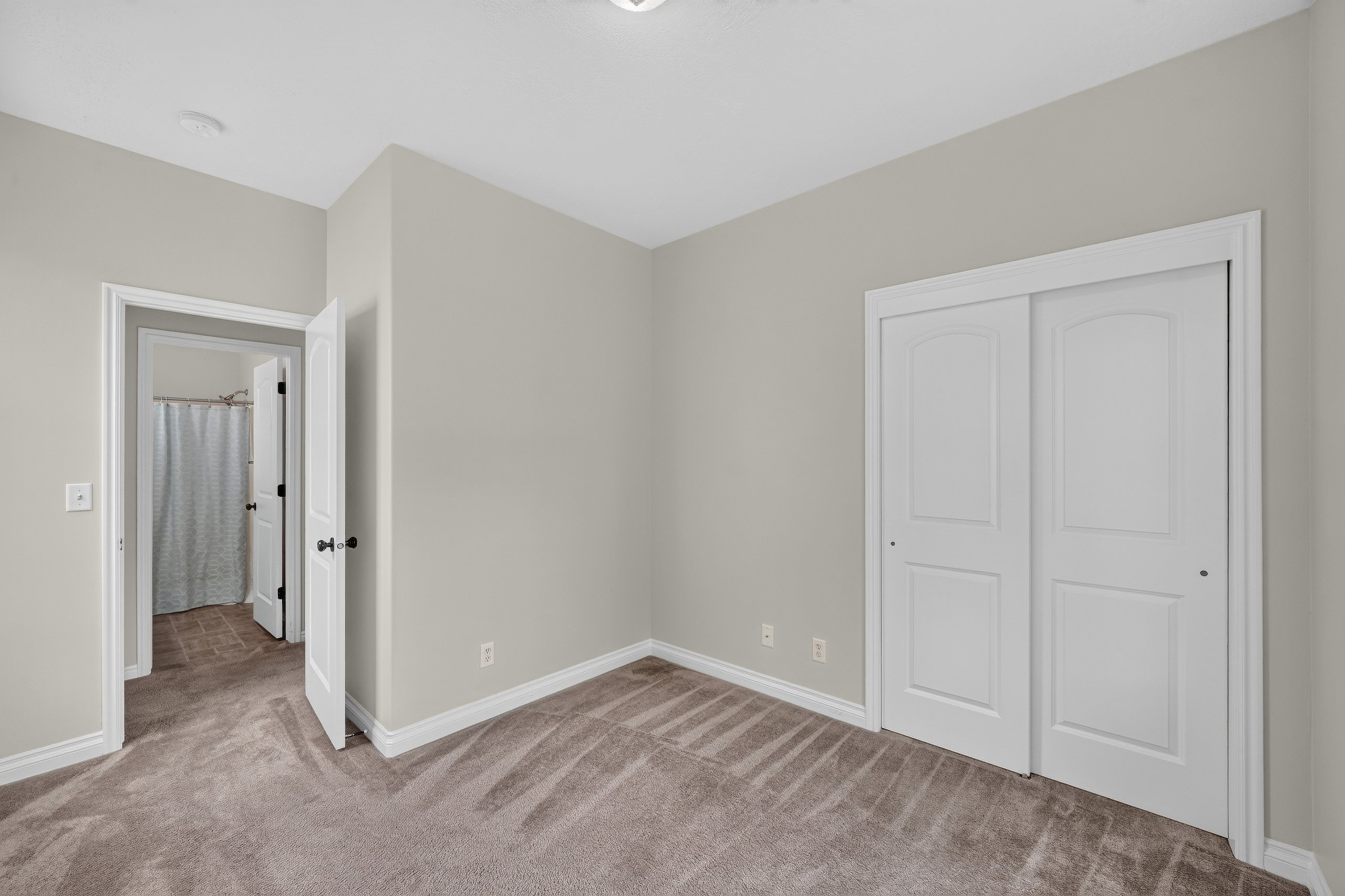 Spacious room featuring neutral wall paint, plush carpet flooring, white trim, and a double-door closet with arch paneling