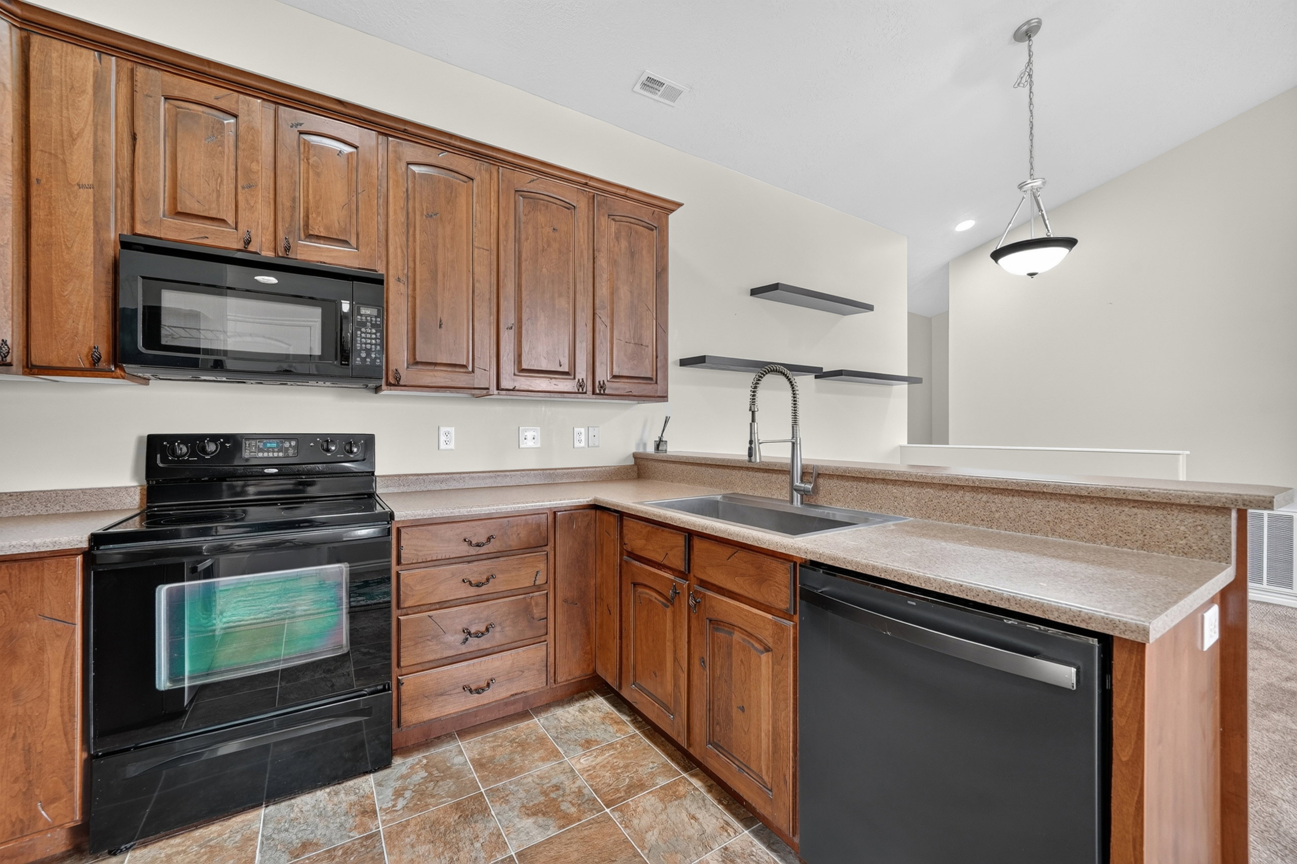 Kitchen featuring wood cabinetry, laminate countertops, a stainless steel sink with a high-arc faucet, black appliances, and tiled flooring