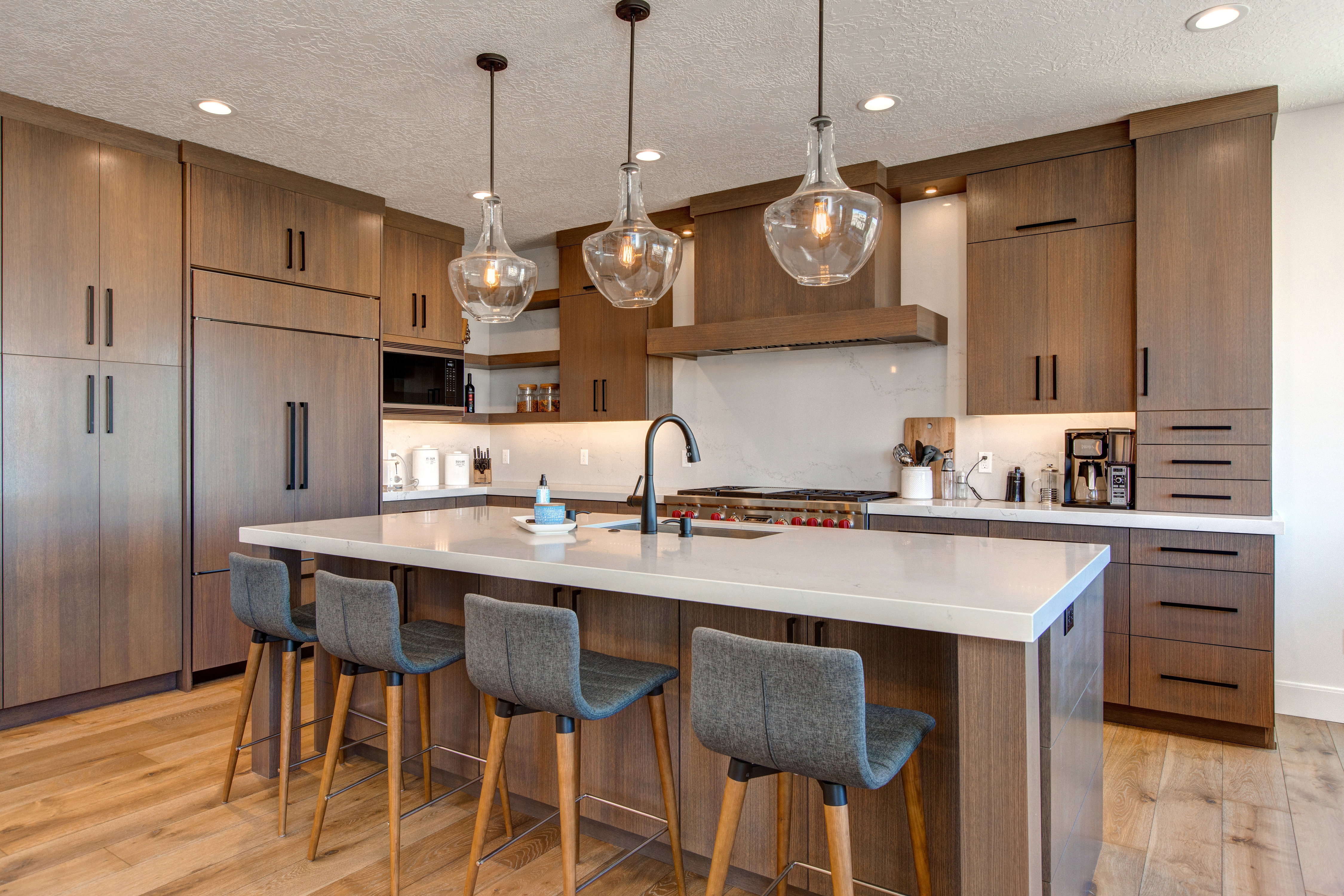 Expansive kitchen featuring a large central island with seating, integrated paneled refrigerator, wood-finish cabinetry, under-cabinet lighting, and three clear glass pendant lights