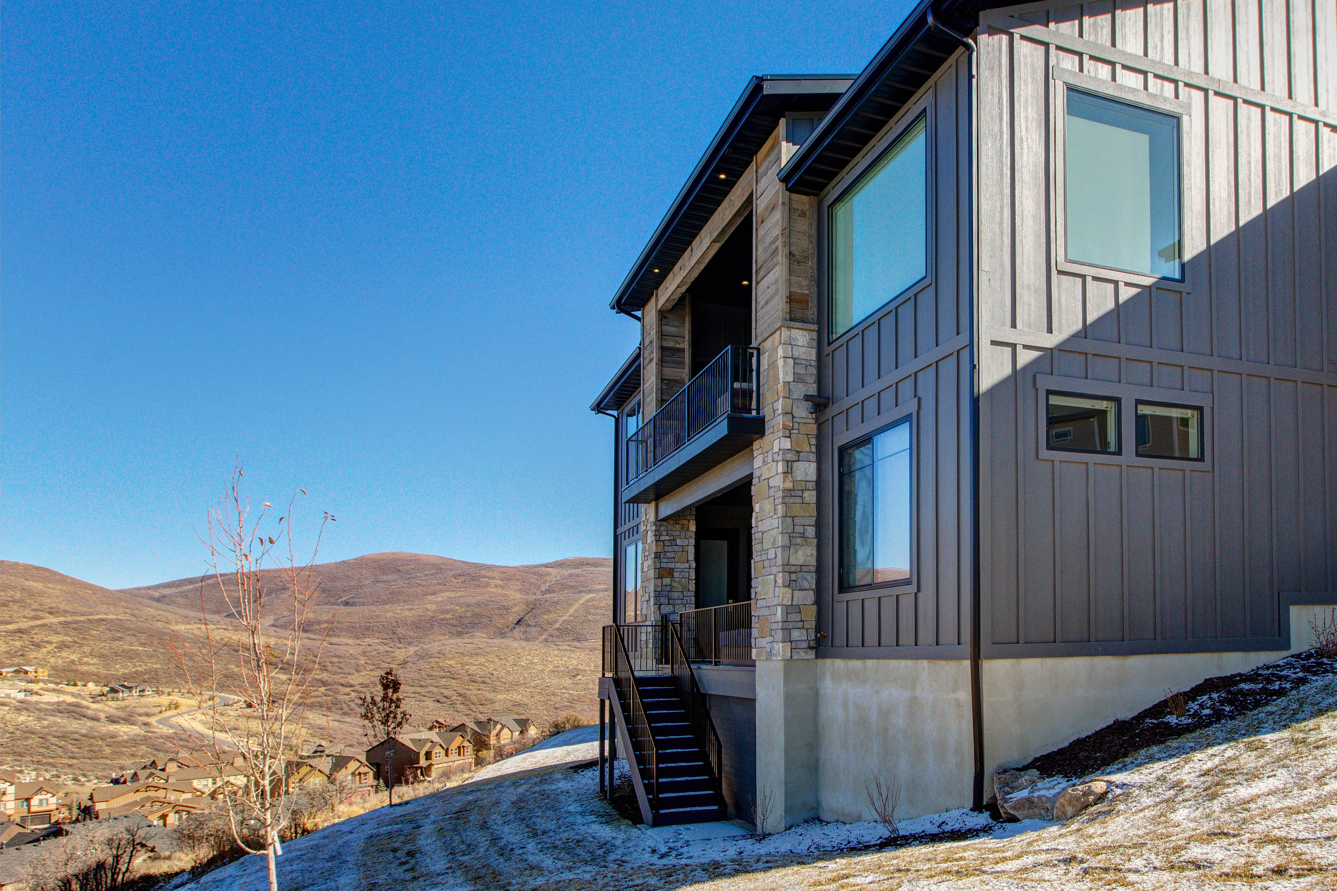 Modern exterior featuring board and batten siding, stone accents, multiple large windows, and a multi-level balcony with a glass railing