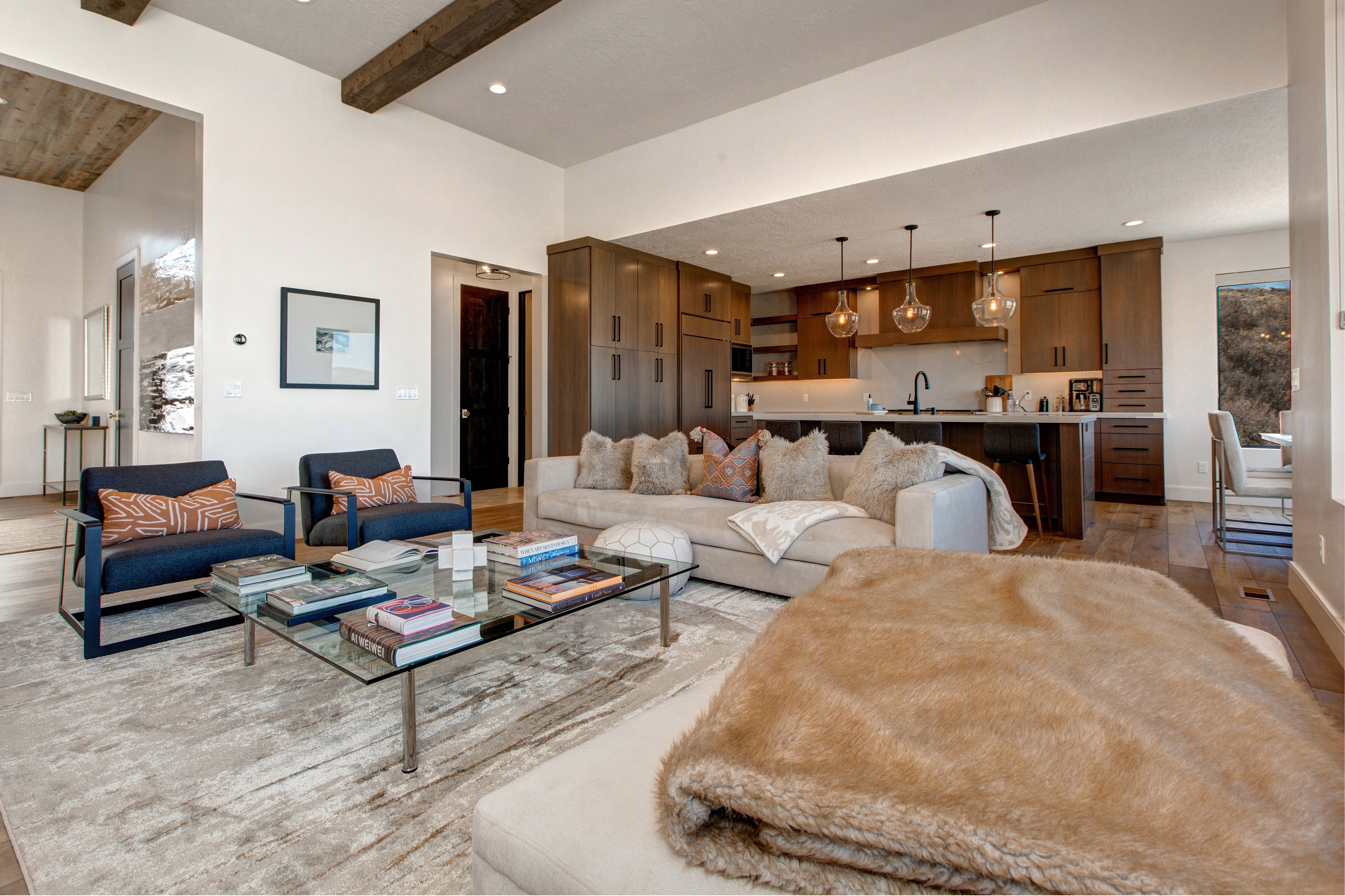Open-concept living space featuring wood-finish flooring, exposed ceiling beams, recessed lighting, a kitchen island with pendant lighting, and abundant cabinetry
