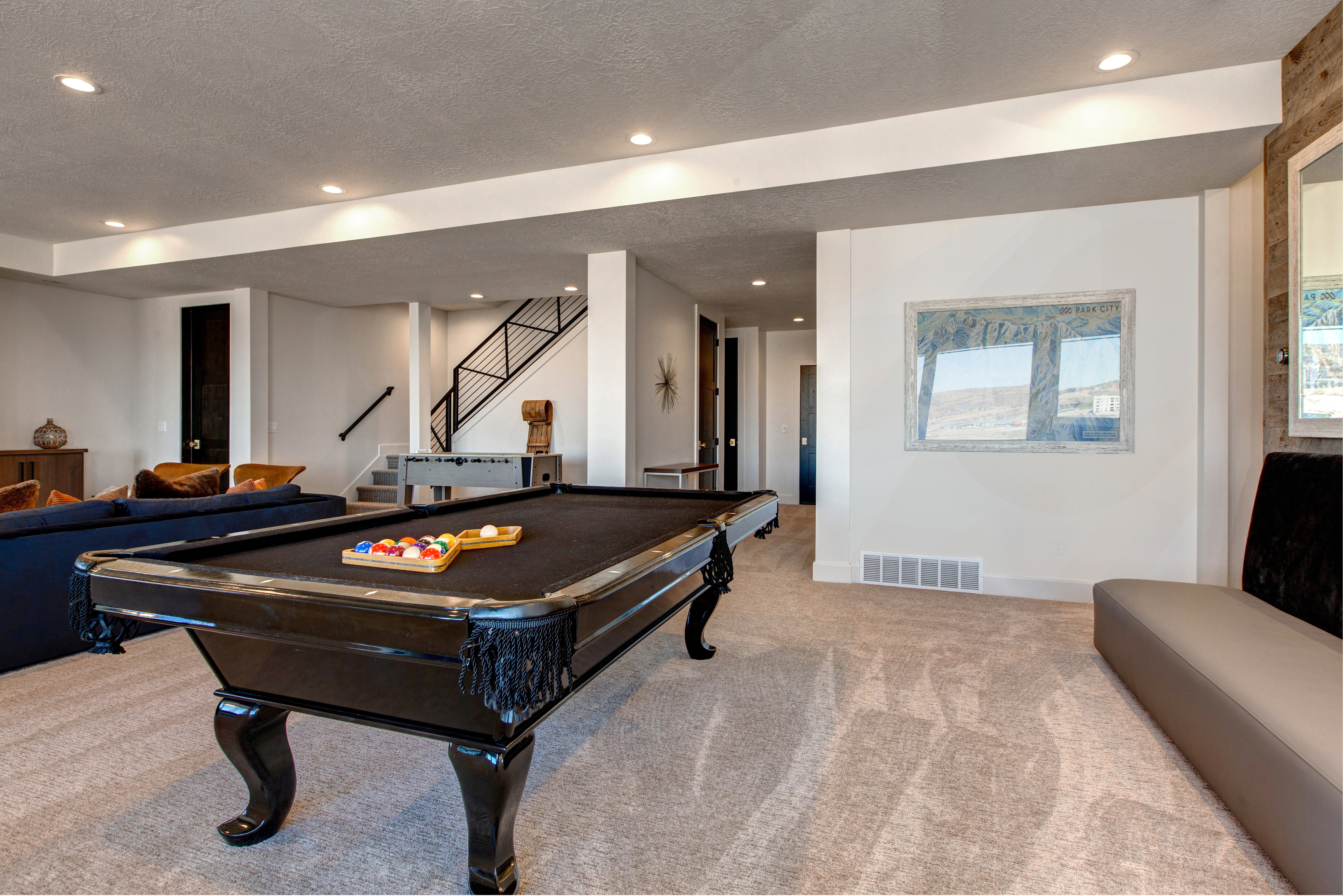 Expansive entertainment area featuring a billiard table, recessed lighting, carpeted flooring, and a contemporary staircase with black railings