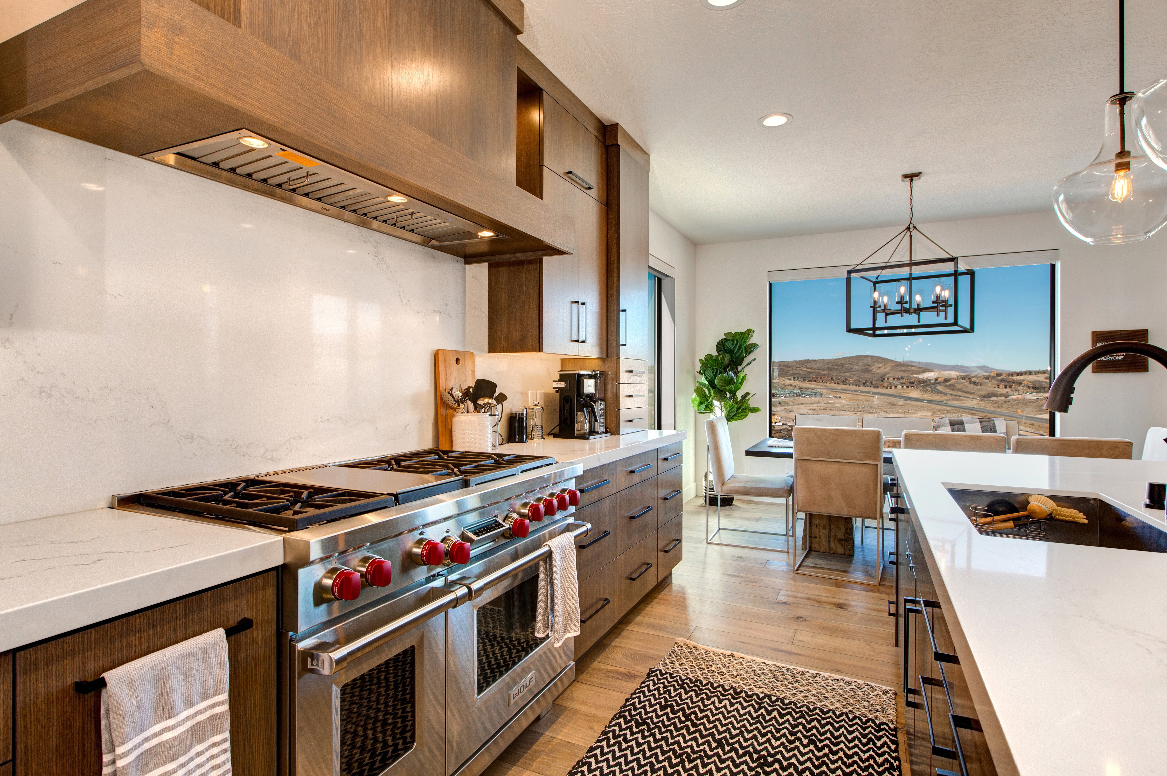 Gourmet kitchen featuring a professional-grade stainless steel range with a custom wood-paneled hood, white countertops, and a full-height white backsplash