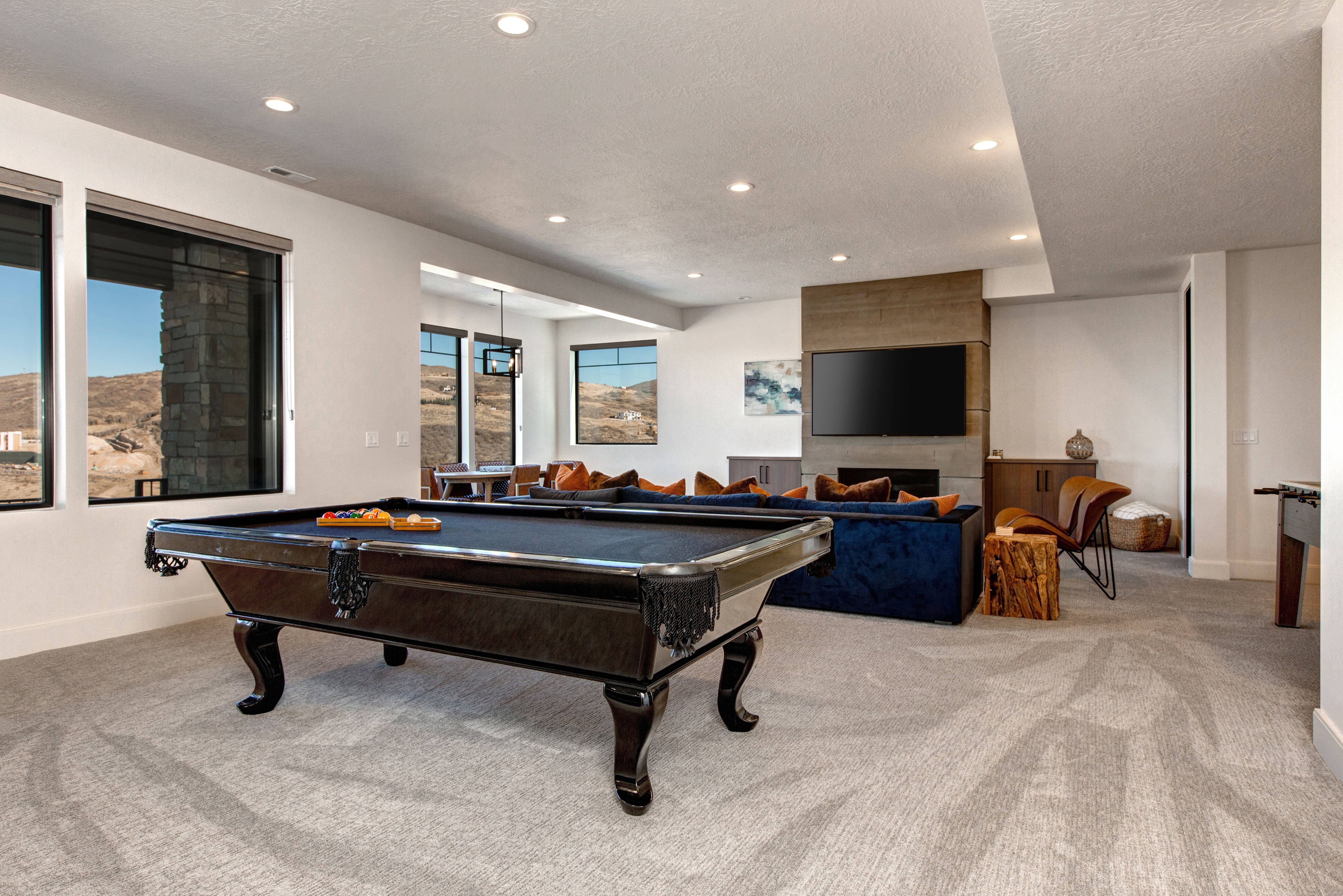 Spacious entertainment room featuring recessed lighting, large windows with roller shades, and a stone-clad fireplace with built-in media space