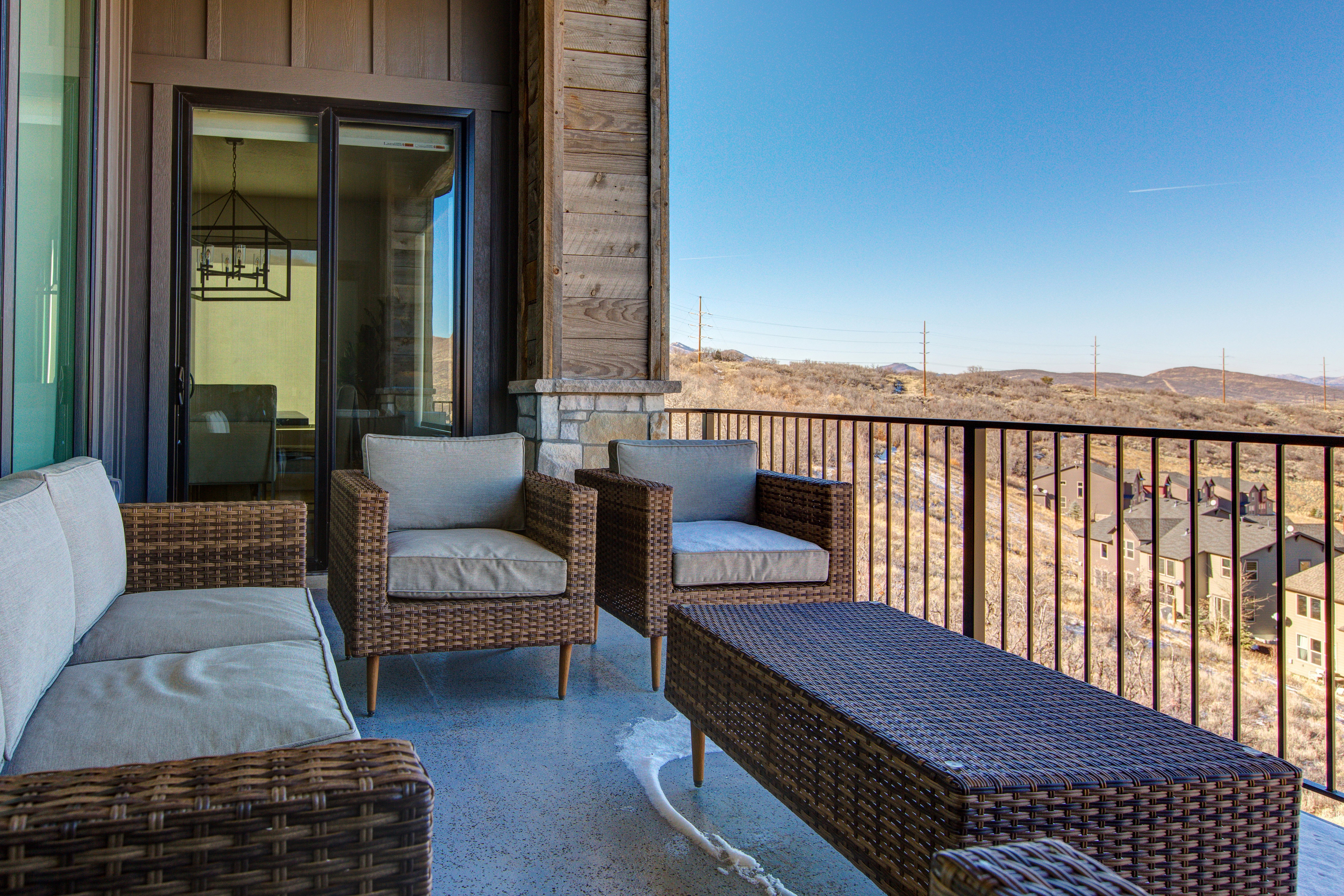 Expansive outdoor patio with concrete flooring, dark metal railing, and a sliding glass door entry