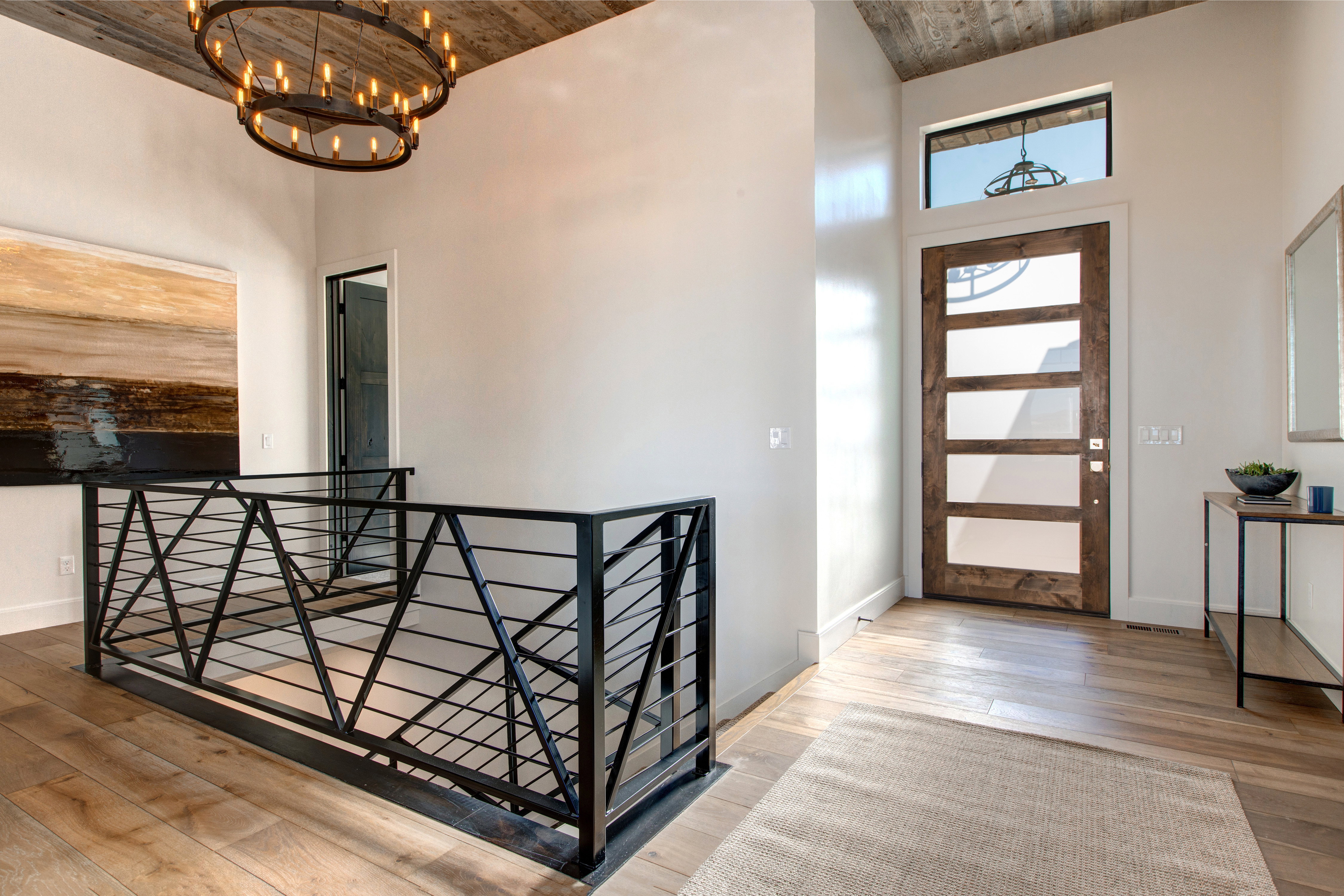 Vaulted ceiling with wood-finish paneling, custom iron chandelier, wood-finish flooring, contemporary front door with clear glass panels, and modern iron railing