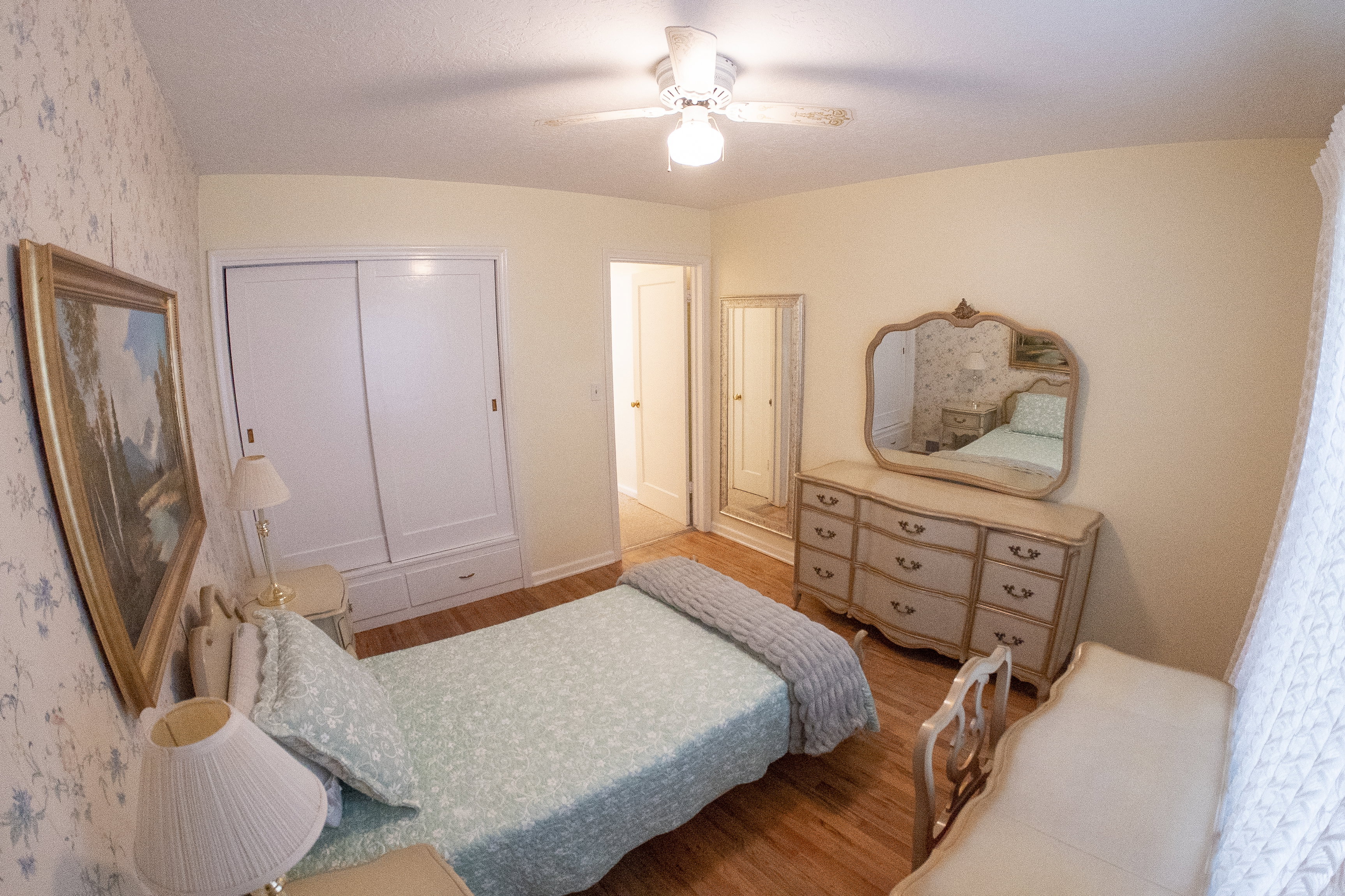 Bedroom featuring light-toned walls, decorative wallpaper, and wood-finish flooring