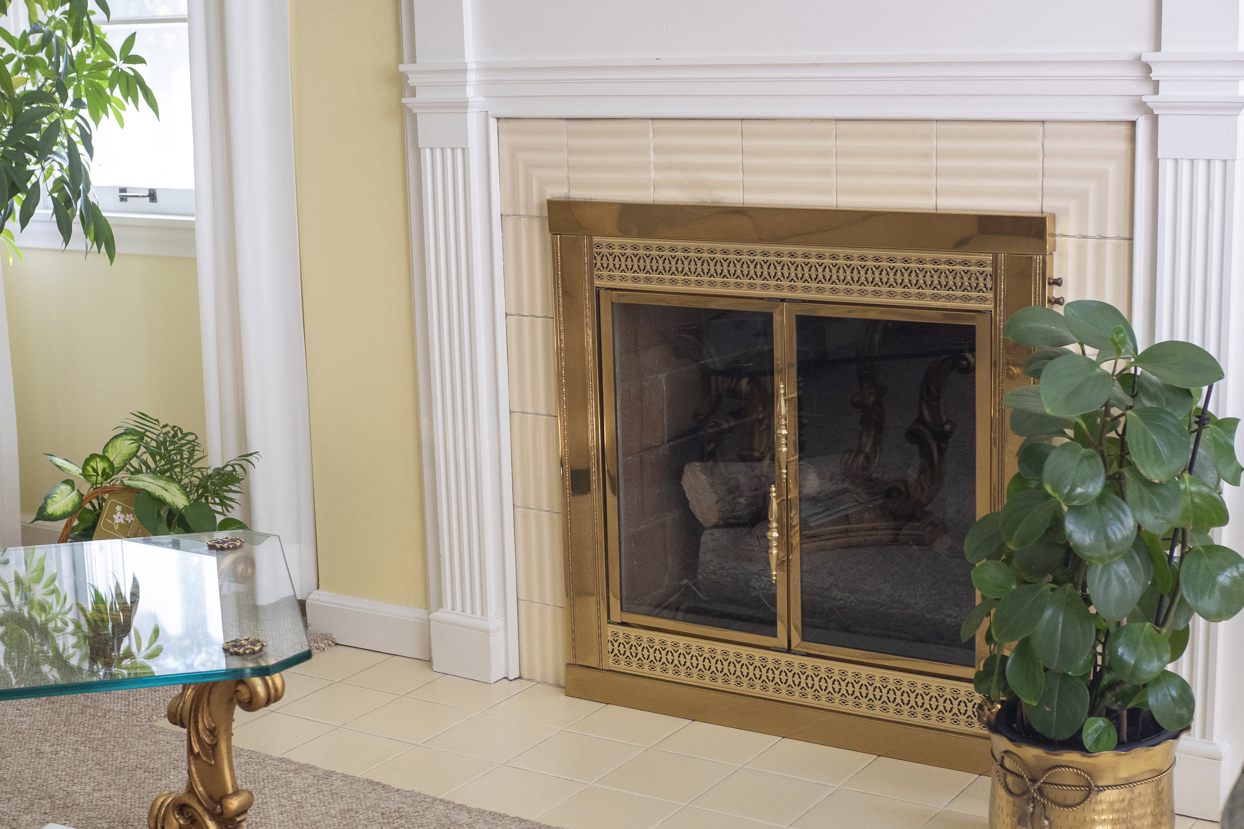 Fireplace featuring a brass frame and glass doors, set within a tiled surround and white mantel with fluted pilasters
