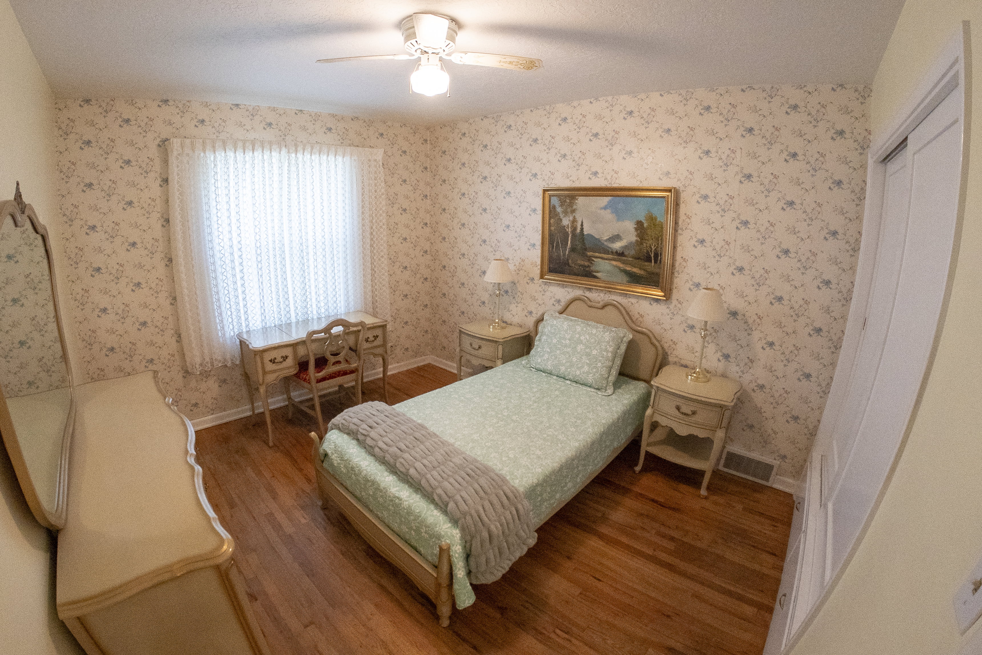 Hardwood flooring throughout featuring a ceiling fan, a window with white blinds, and floral wallpaper