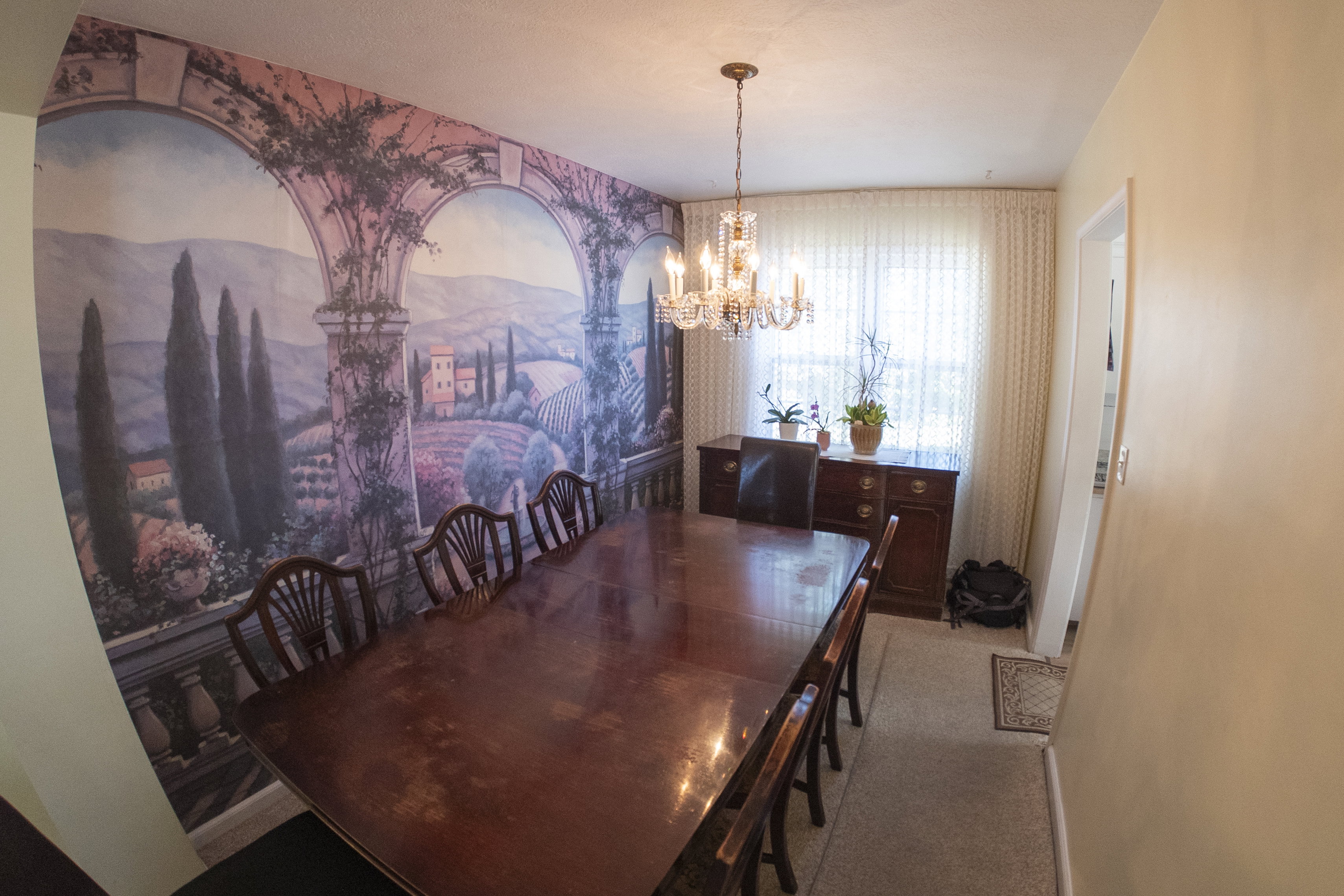 Dining area featuring a mural accent wall, hardwood-finish dining table, and a crystal chandelier