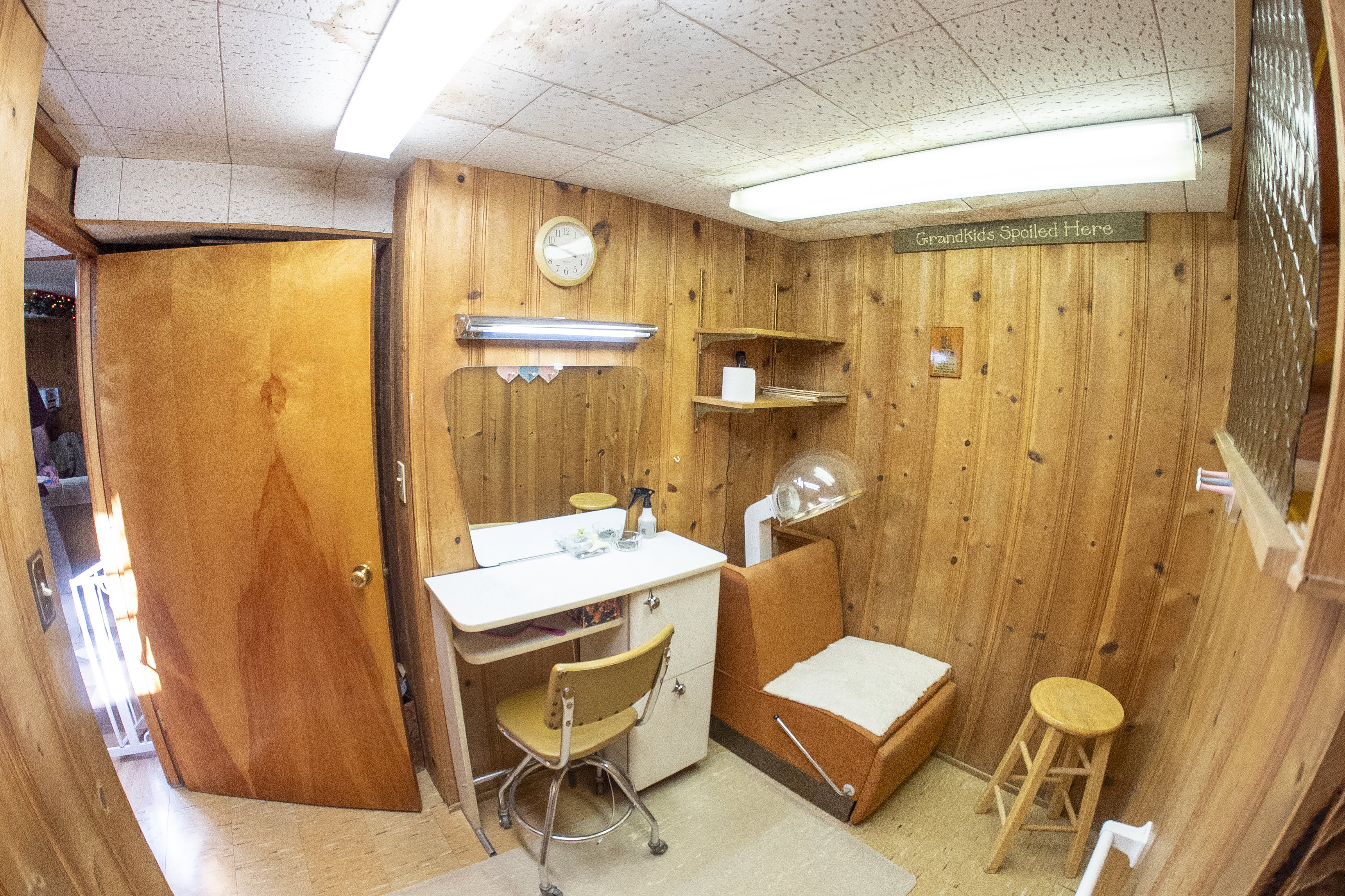 Wood-paneled room featuring a built-in vanity with mirror and overhead lighting, wall-mounted shelving, and recessed ceiling lights