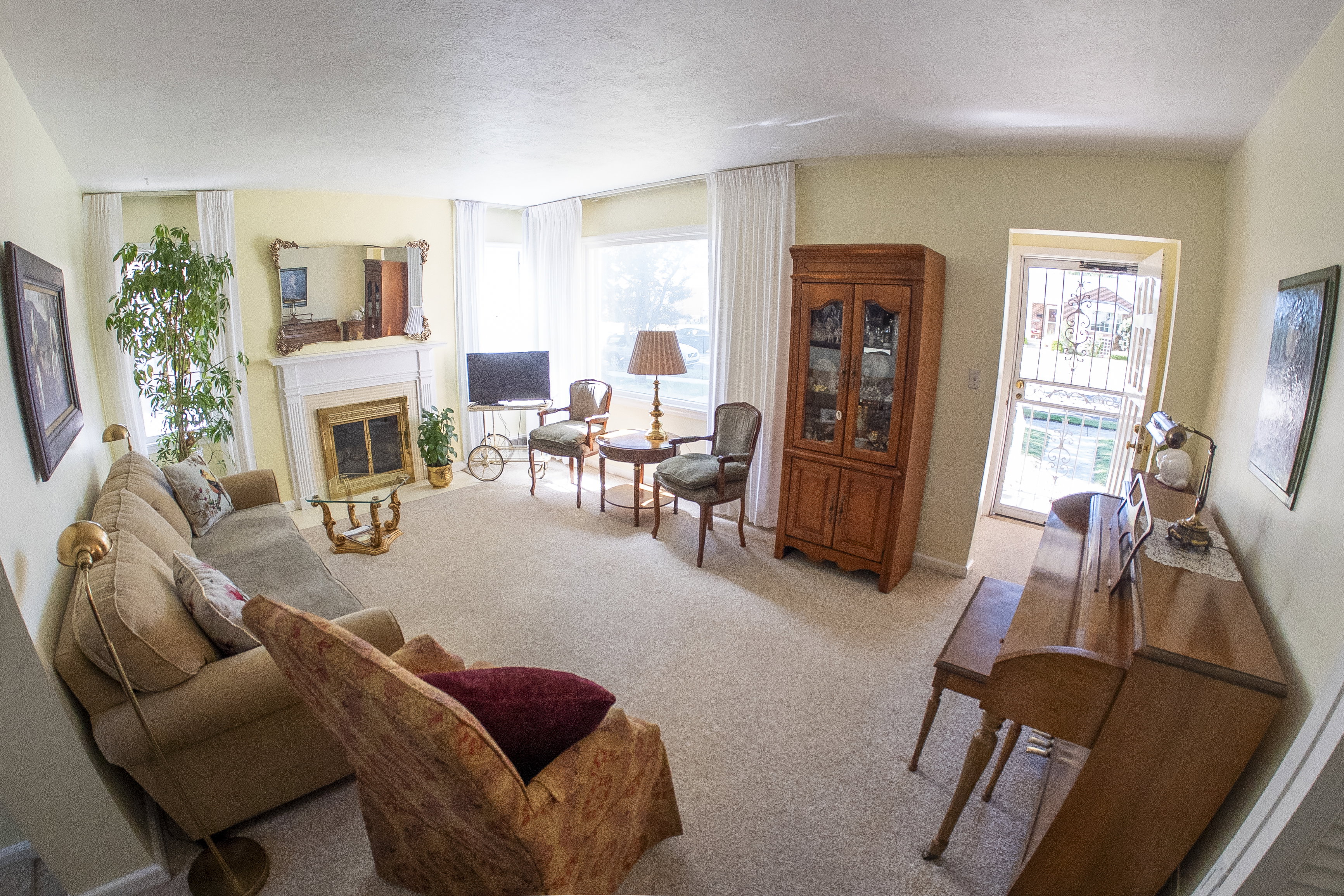 Carpeted living area featuring a fireplace with a white mantel, multiple large windows, and a front entry door with a decorative security gate