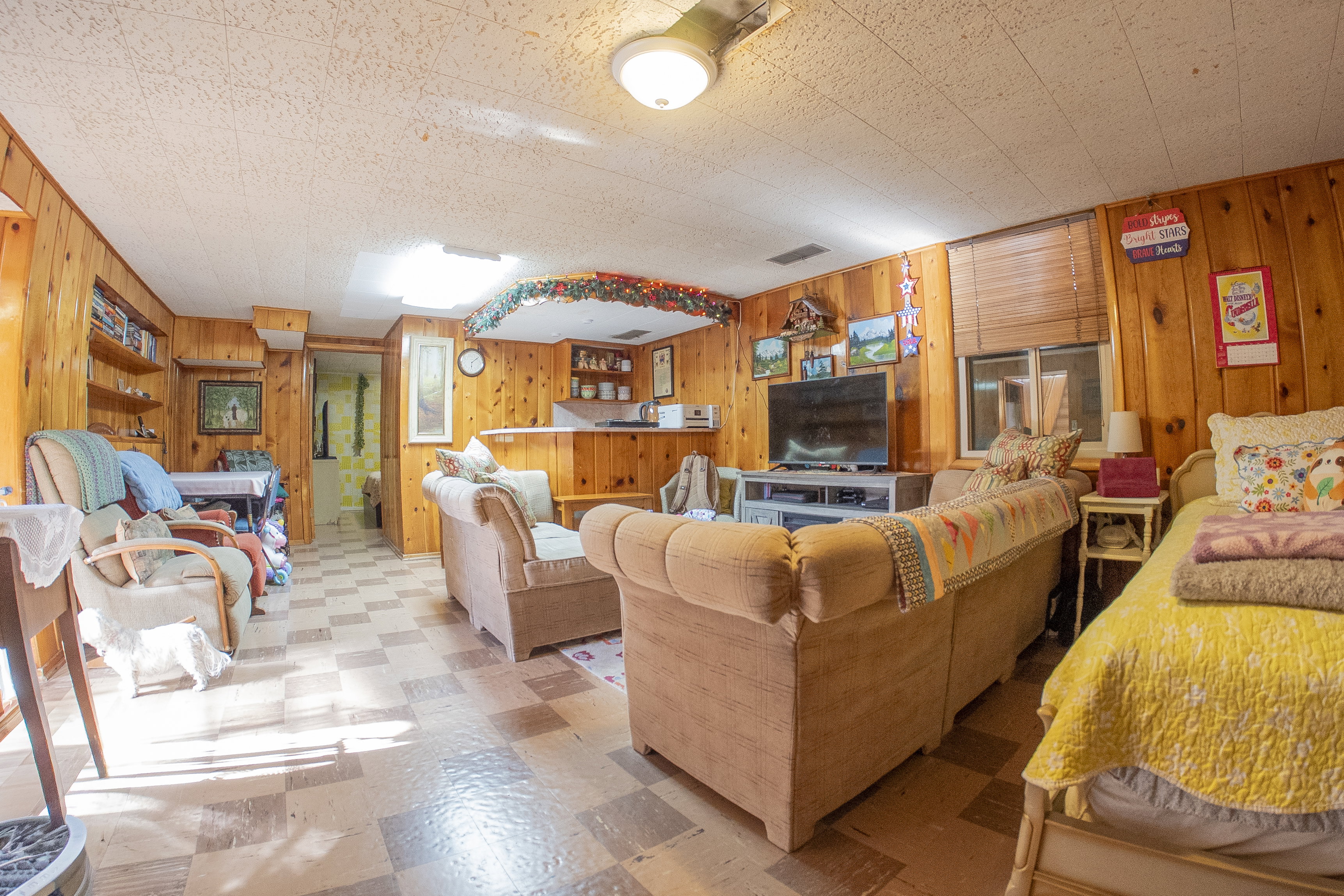 Wood paneling throughout this living space featuring built-in shelving, a wet bar, and a window with horizontal blinds