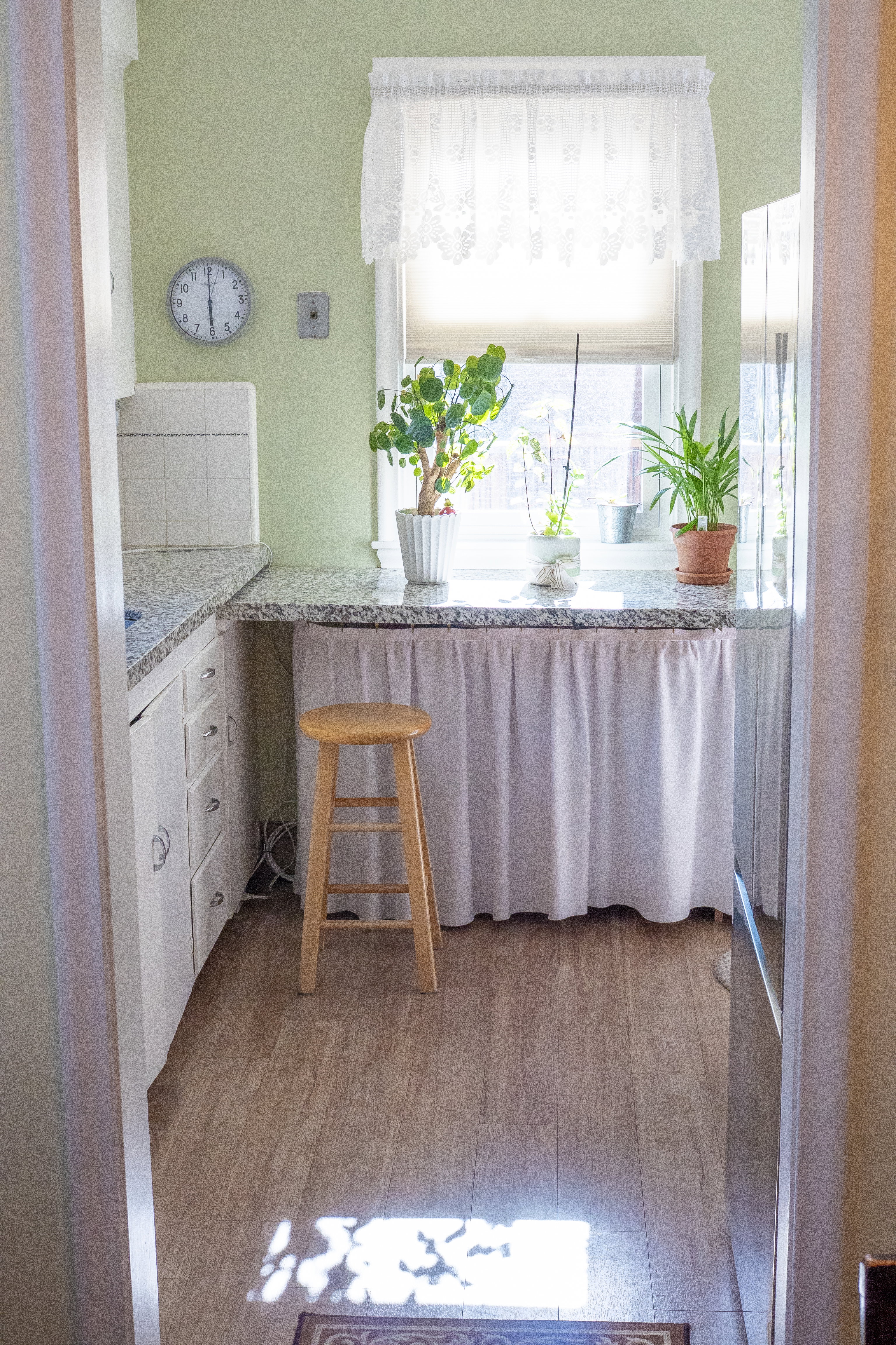 Kitchenette area featuring a window, granite-style countertops, white cabinetry, wood-finish flooring, and light green walls