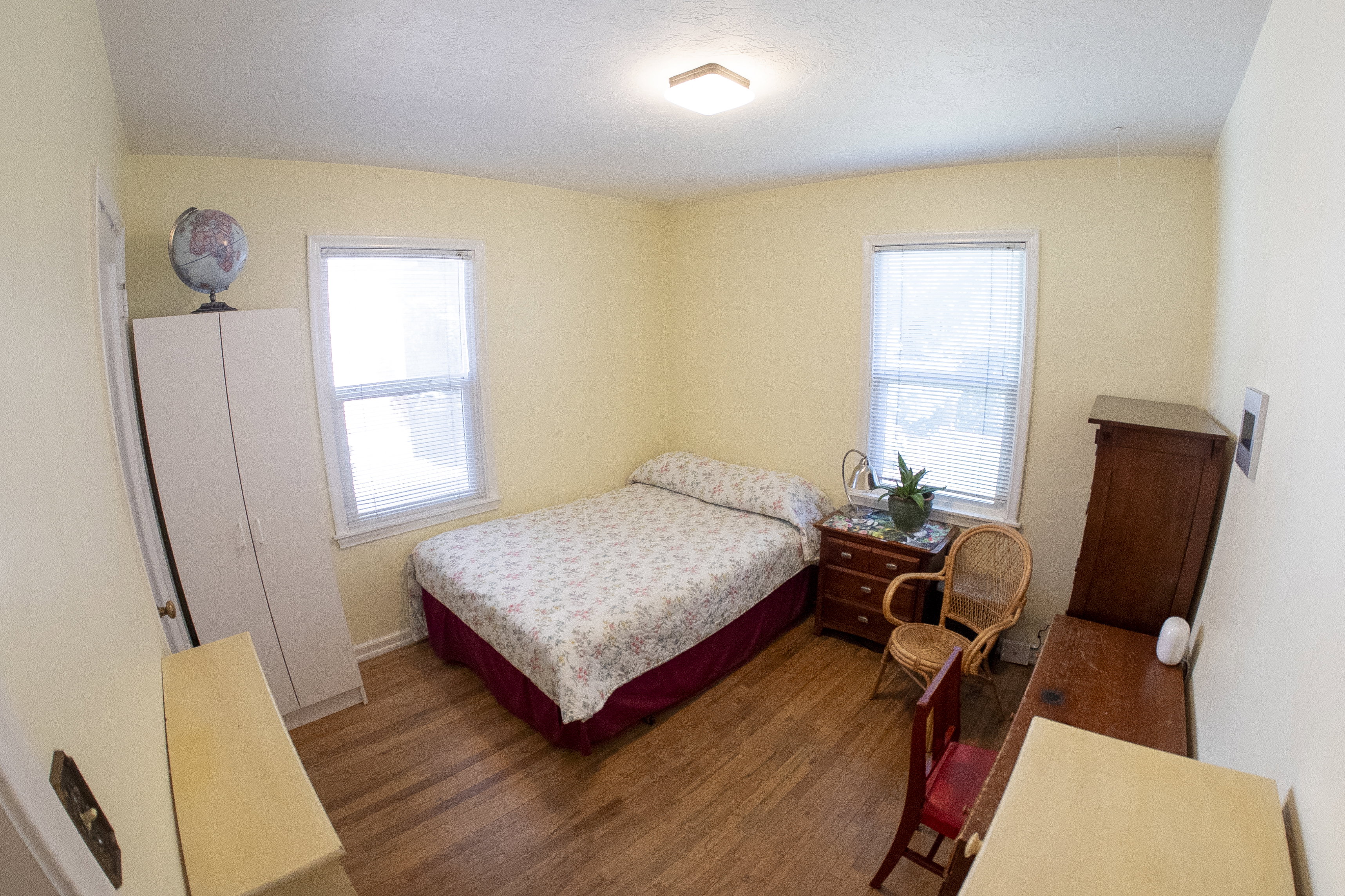 Room featuring wood-finish flooring, two windows with blinds, light yellow walls, and a ceiling-mounted light fixture