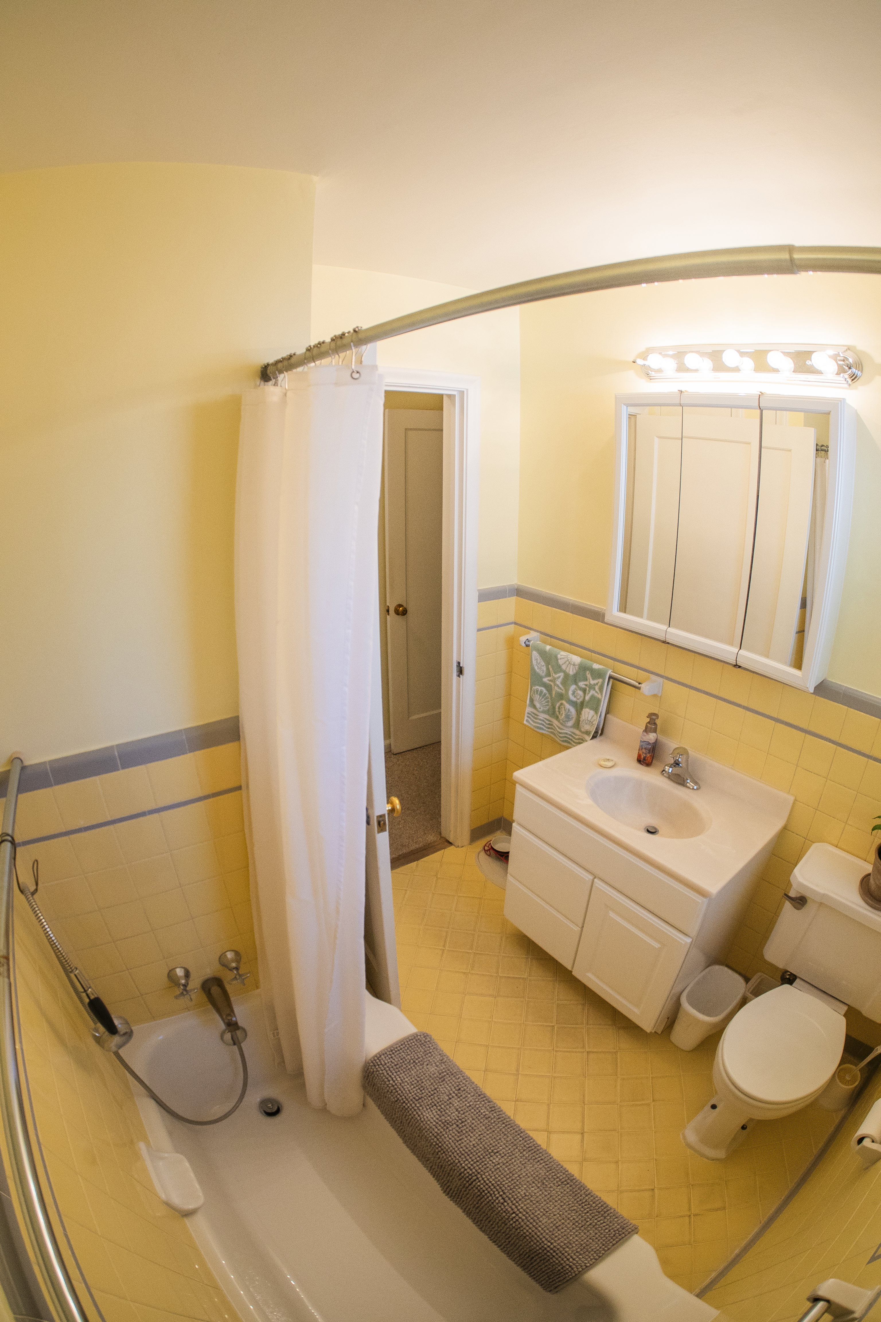 Bathroom featuring yellow tile flooring, yellow wall tile with blue accent trim, and a white bathtub with a curved shower rod