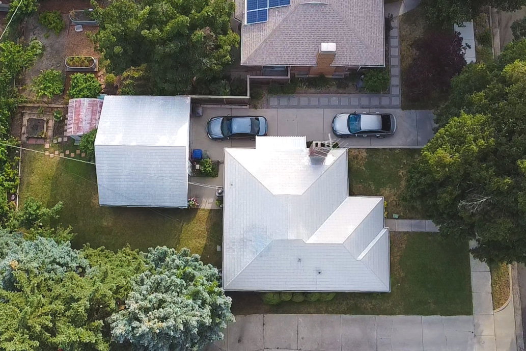 Aerial view showcasing a property with a light-colored, multi-gabled roof and a detached structure featuring a similar roof