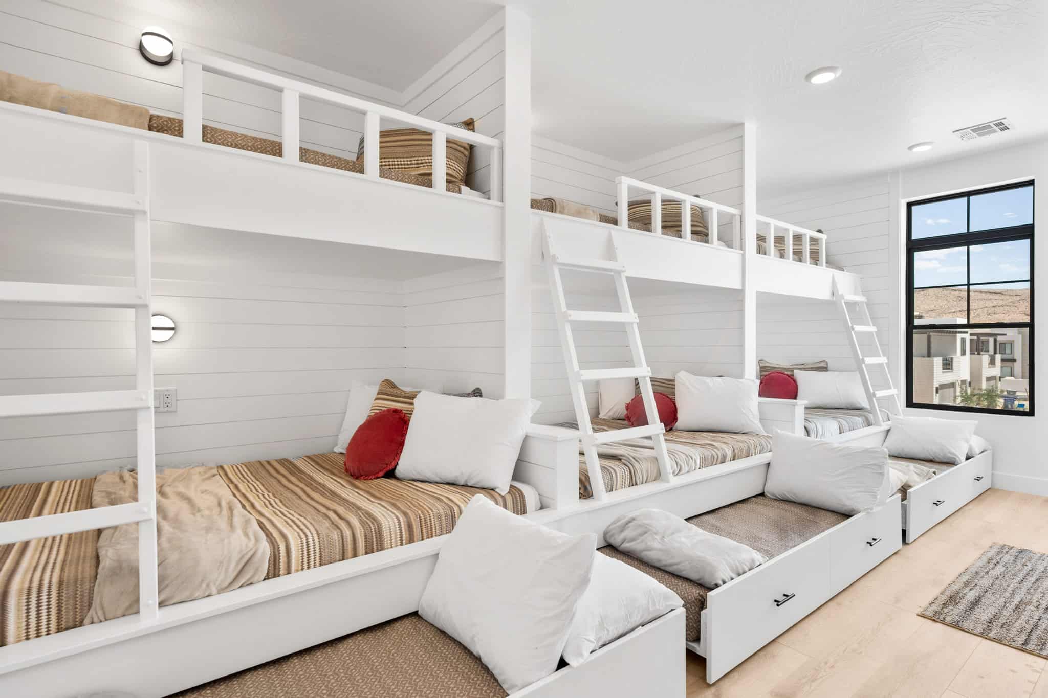 Built-in bunk beds featuring integrated lighting, shiplap wall finishes, natural wood-finish flooring, and a large black-framed window