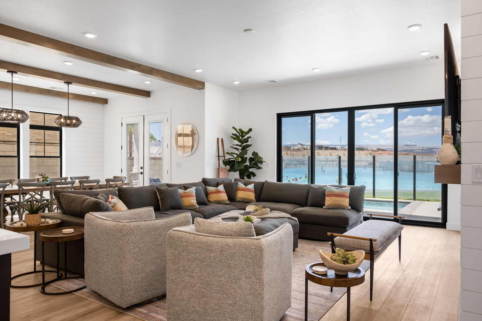 Open-concept living area featuring light wood-finish flooring, white shiplap accent wall, and exposed wood ceiling beams