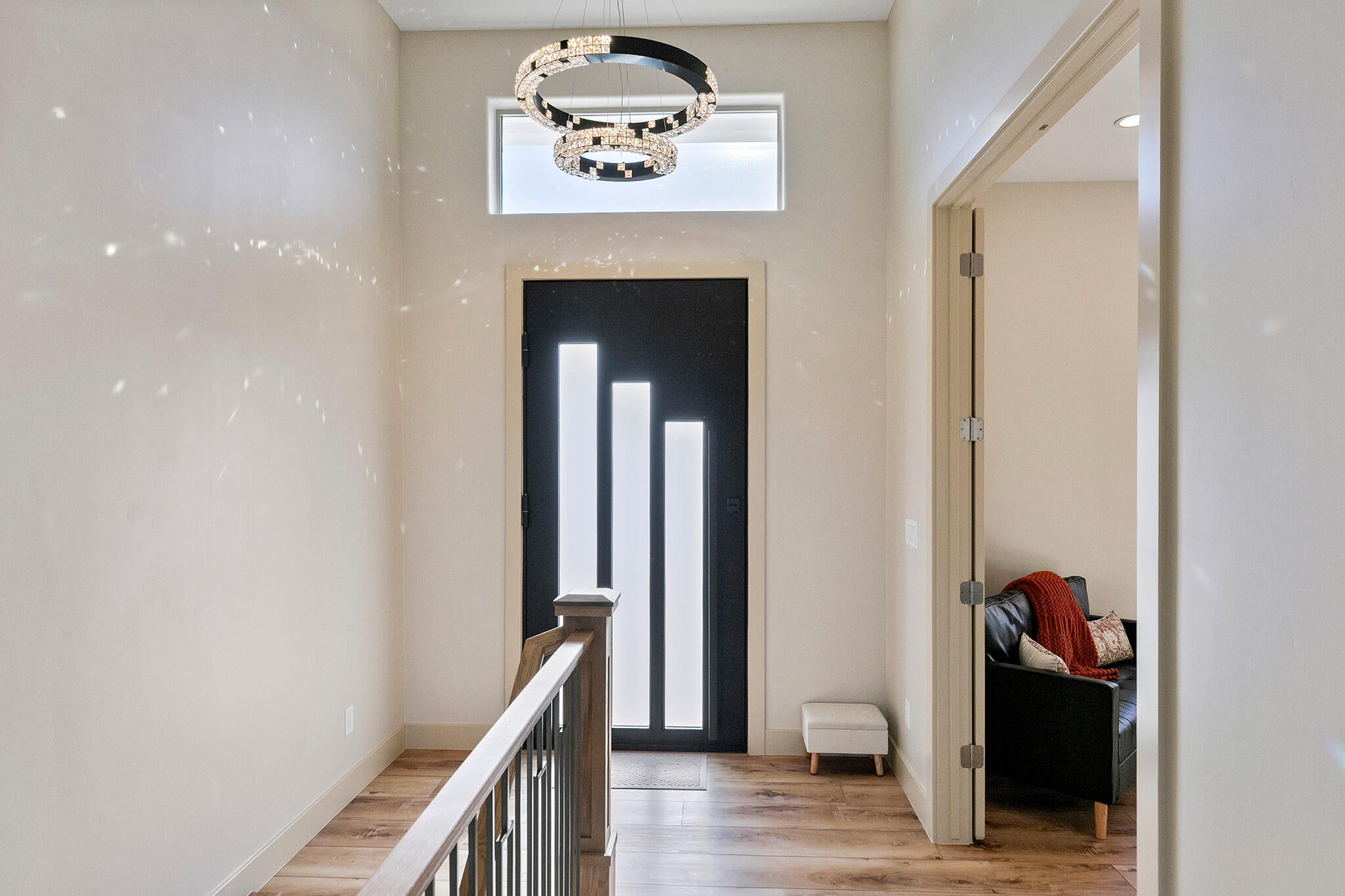 Entryway featuring a modern black door with vertical glass inserts, transom window, contemporary chandelier, wood-finish flooring, and a staircase with a wooden handrail and metal balusters