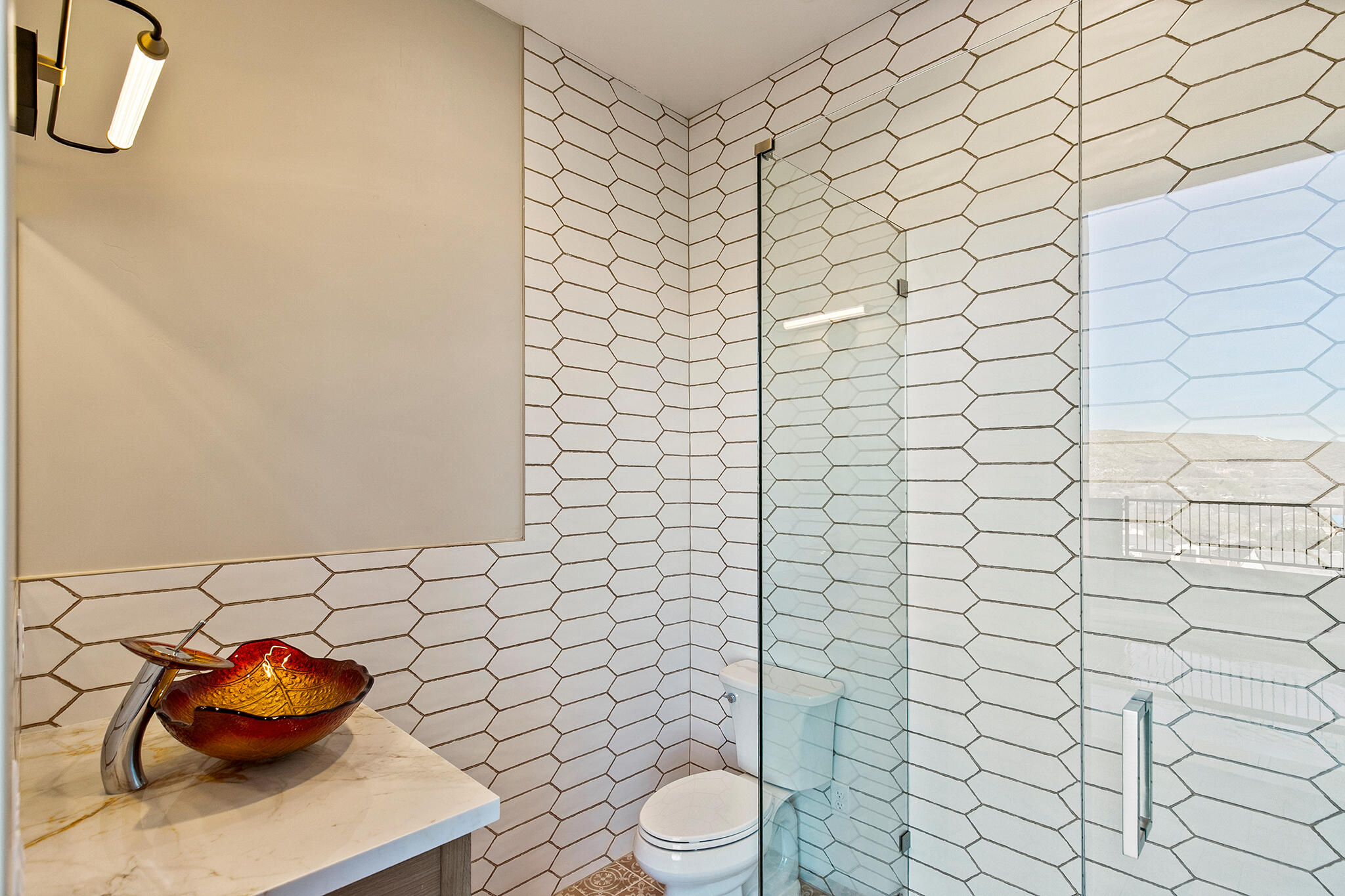 Modern bathroom featuring an enclosed shower with a clear glass door, white elongated hexagonal tile walls, and a light-colored vanity with a vessel sink