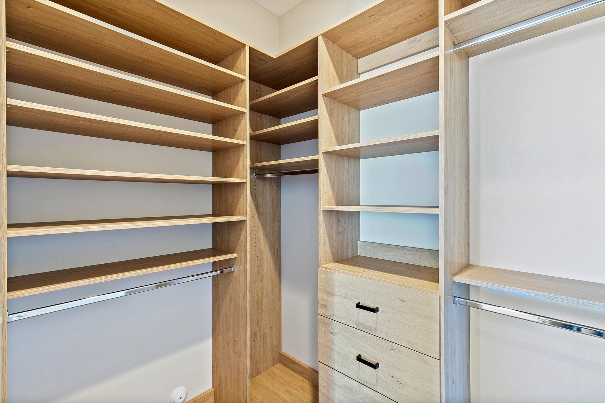 Custom closet system featuring wood-finish shelving, built-in drawers with dark hardware, and chrome hanging rods