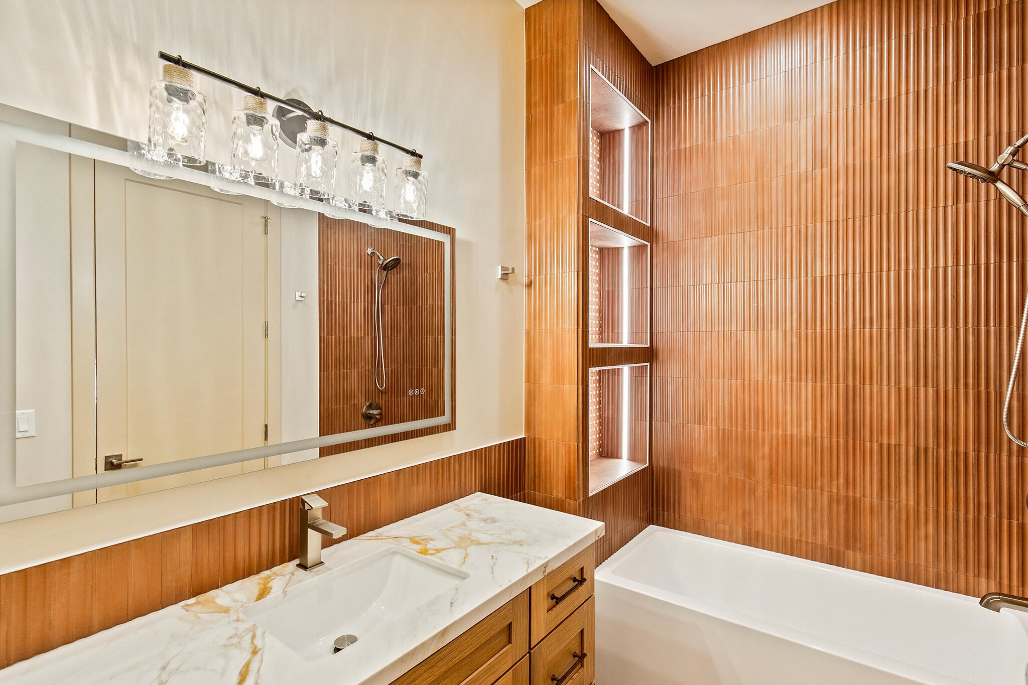 Bathroom featuring a white rectangular undermount sink, a marble-patterned countertop, light wood cabinetry with dark hardware, and a chrome faucet
