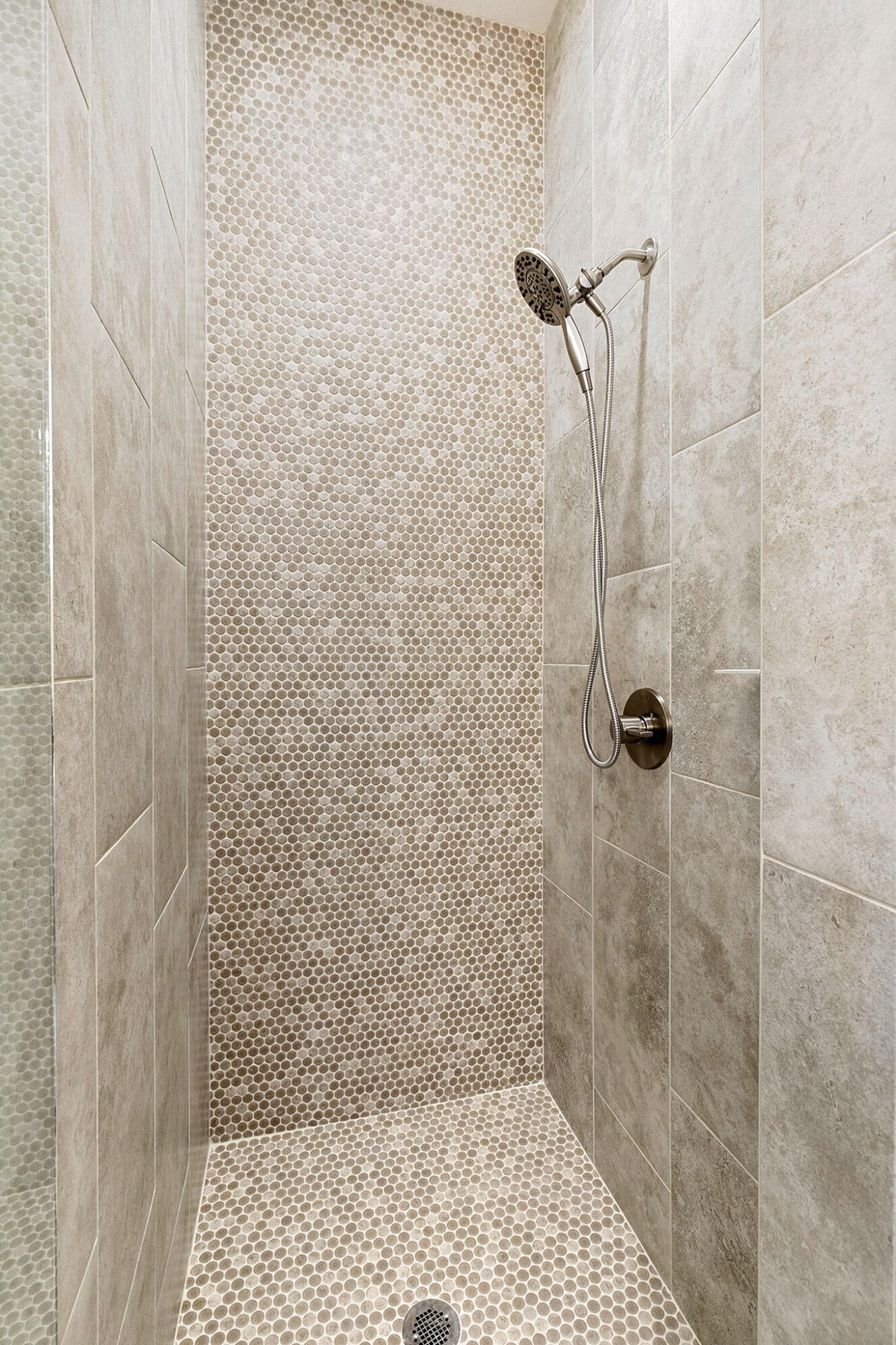 Shower enclosure featuring large format wall tiles, penny tile accent wall, penny tile shower floor, and a brushed nickel shower head with handheld attachment