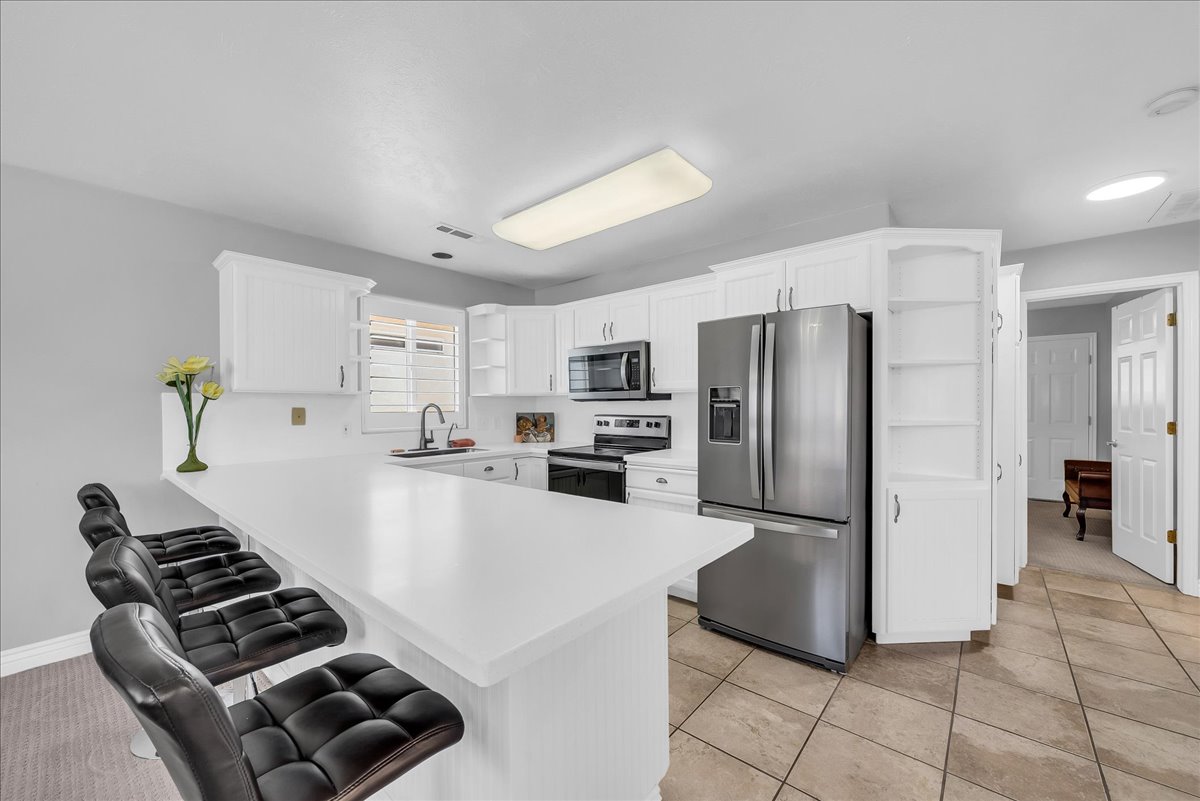 Kitchen featuring a large breakfast bar, white cabinetry, stainless steel appliances, and tile flooring