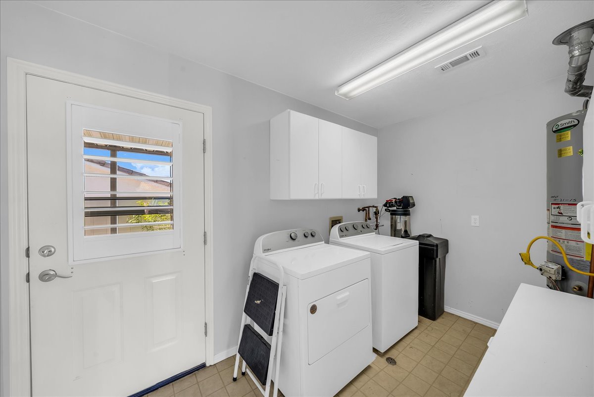 Utility space featuring a water heater, white cabinetry, and light-colored tile flooring