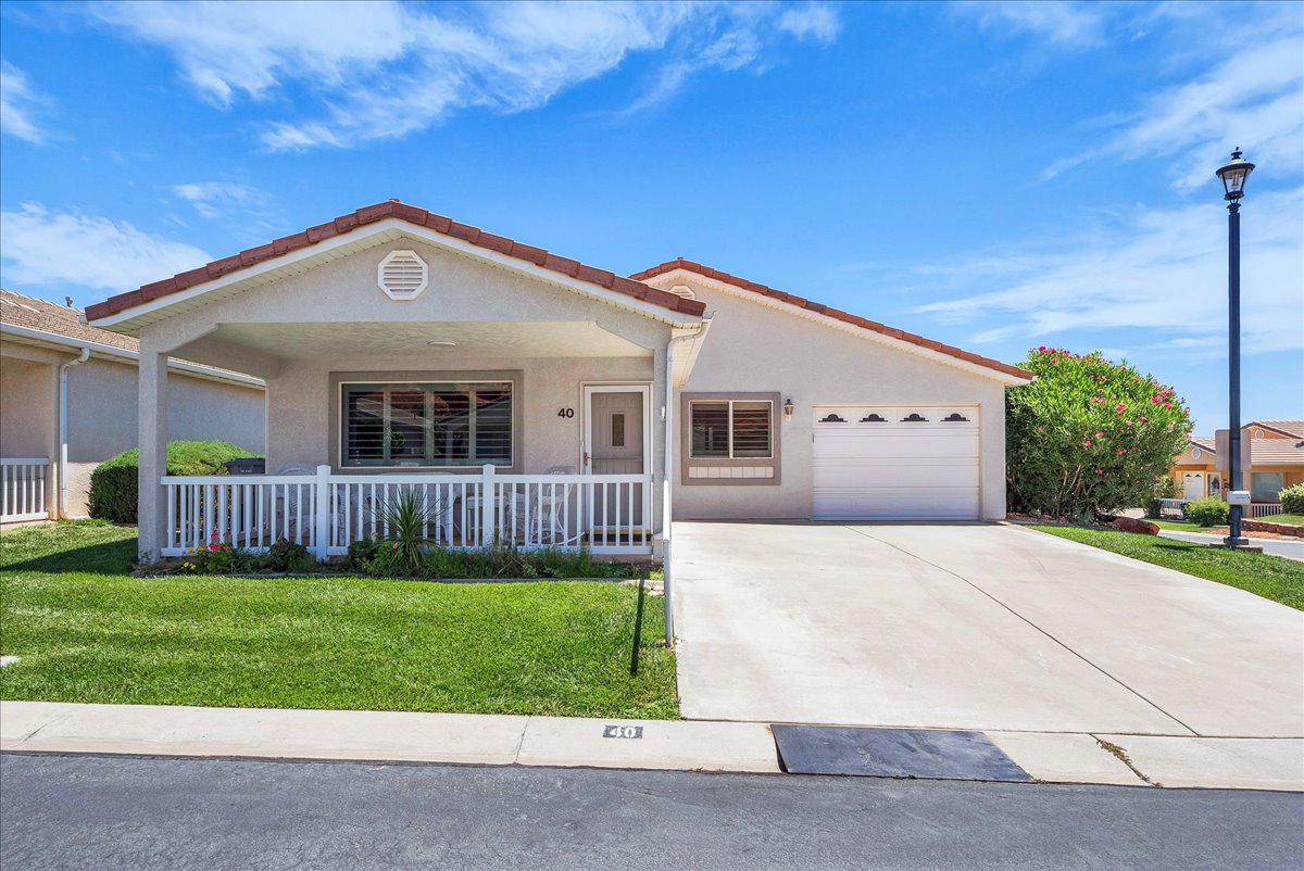 Single-story home featuring a covered front porch, white picket railing, attached two-car garage, concrete driveway, and manicured front lawn